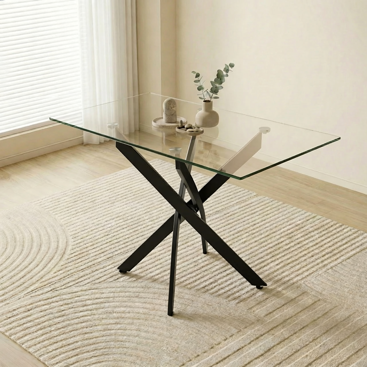 Three-quarter view of the glass dining table with black crossed legs near a window with eucalyptus