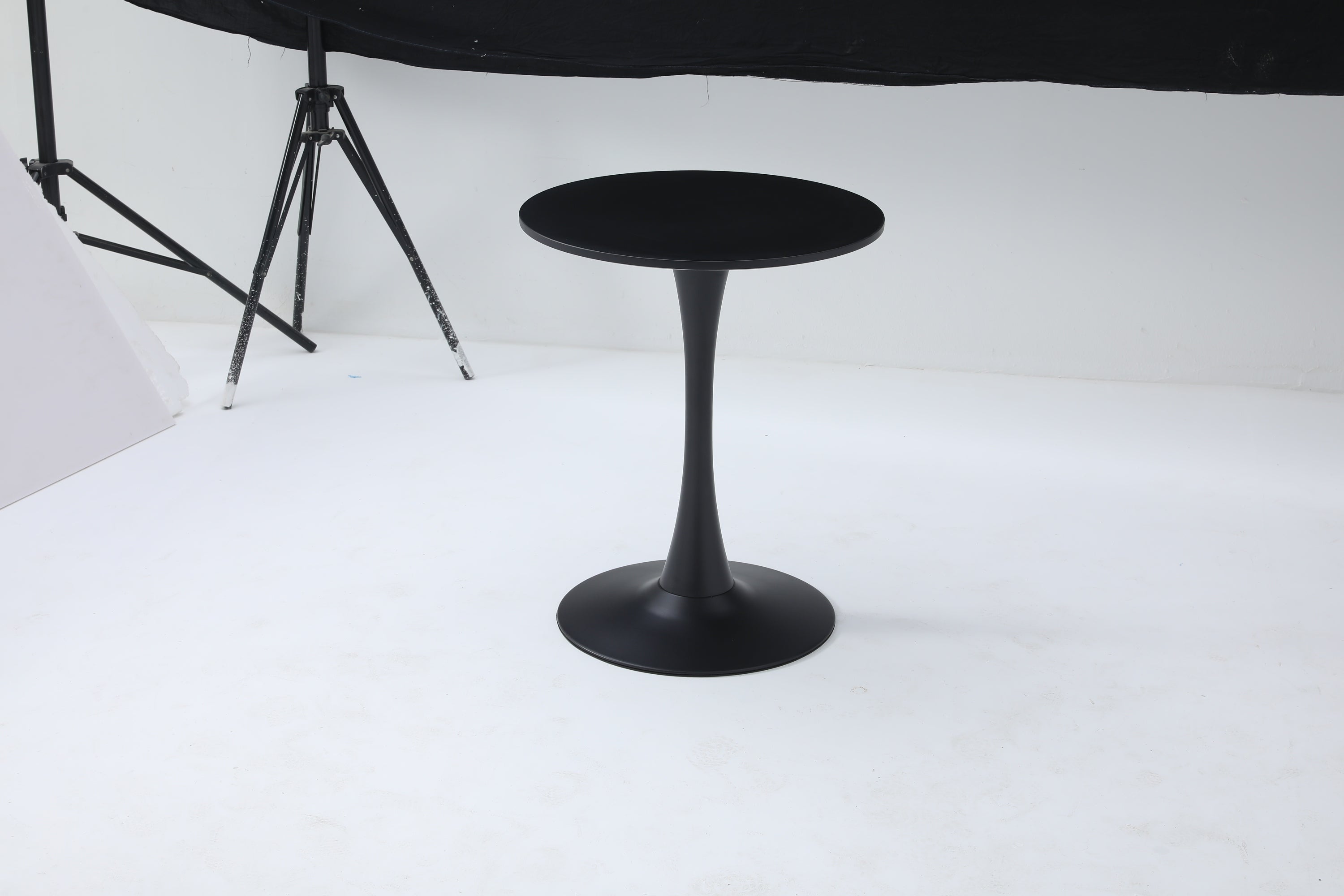Black round bistro table with tulip pedestal on a studio floor with lighting equipment