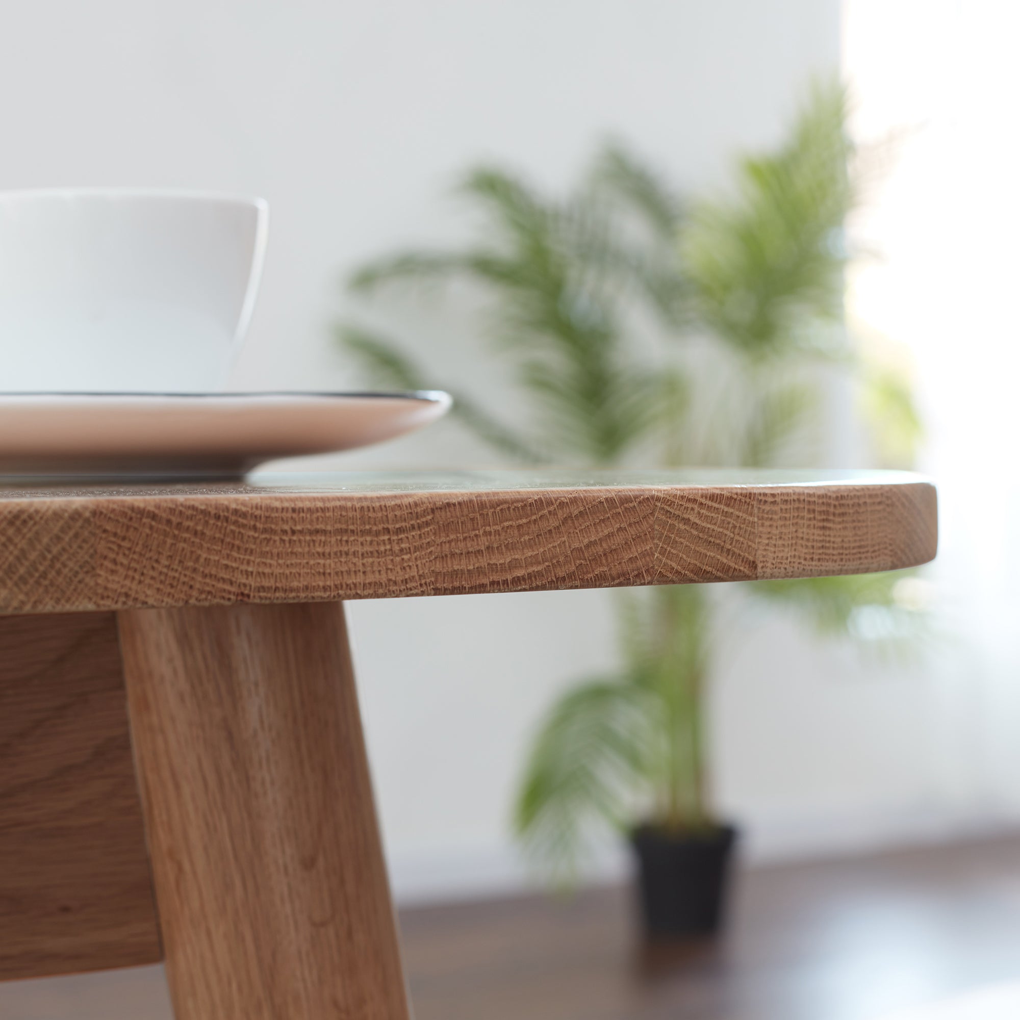 Close-up of the oak tabletop corner with a cup and saucer, plant in the background