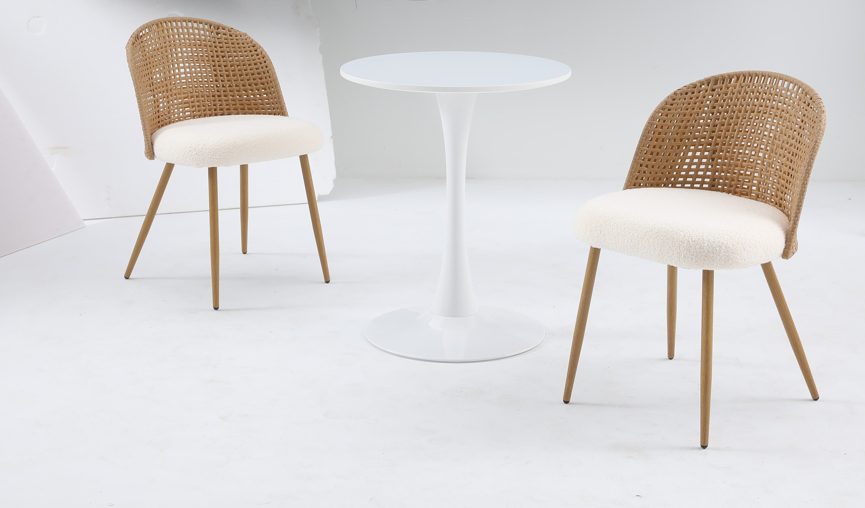 White round bistro table set with two rattan-back chairs in a studio setting