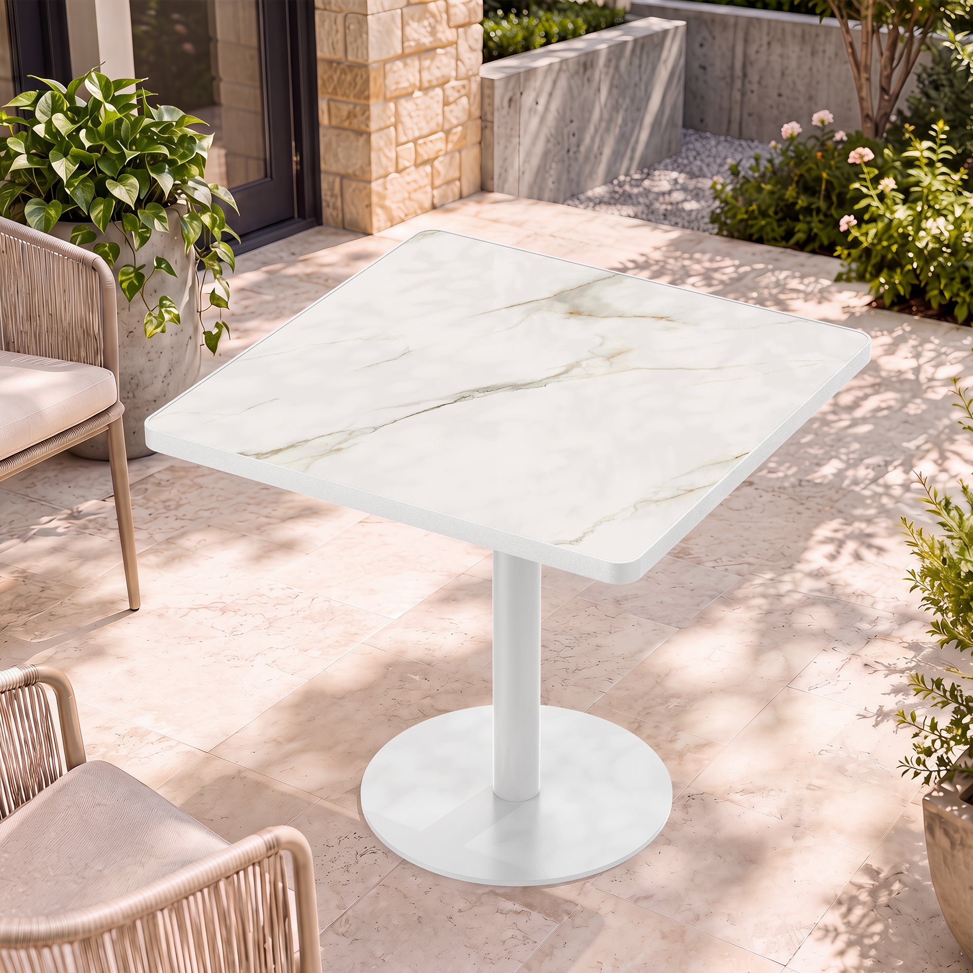 White marble-look square dining table on a sunny stone patio with woven chairs and plants