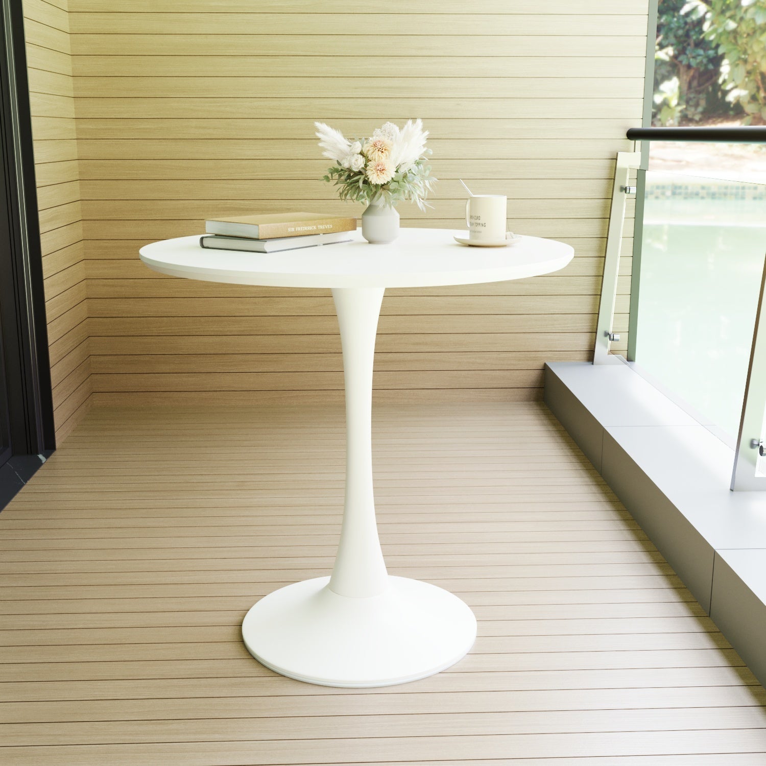 White tulip dining table on a wood deck beside a glass railing, styled with books and a vase