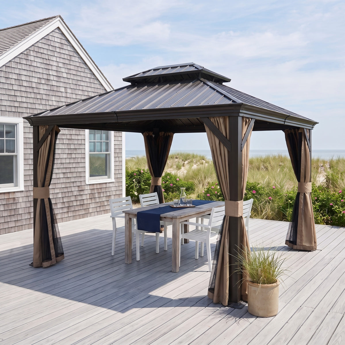 Dark brown hardtop gazebo with tan curtains over a dining table on a gray deck by the beach in daylight