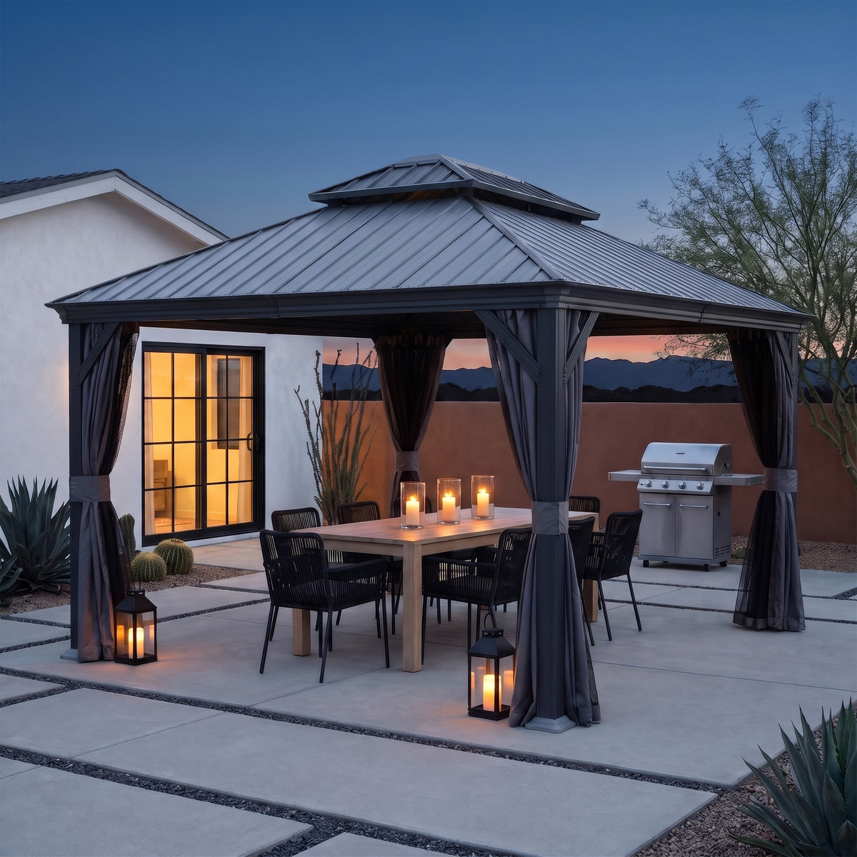 Dark gray double roof hardtop gazebo with curtains tied back over a dining table on a desert patio at dusk