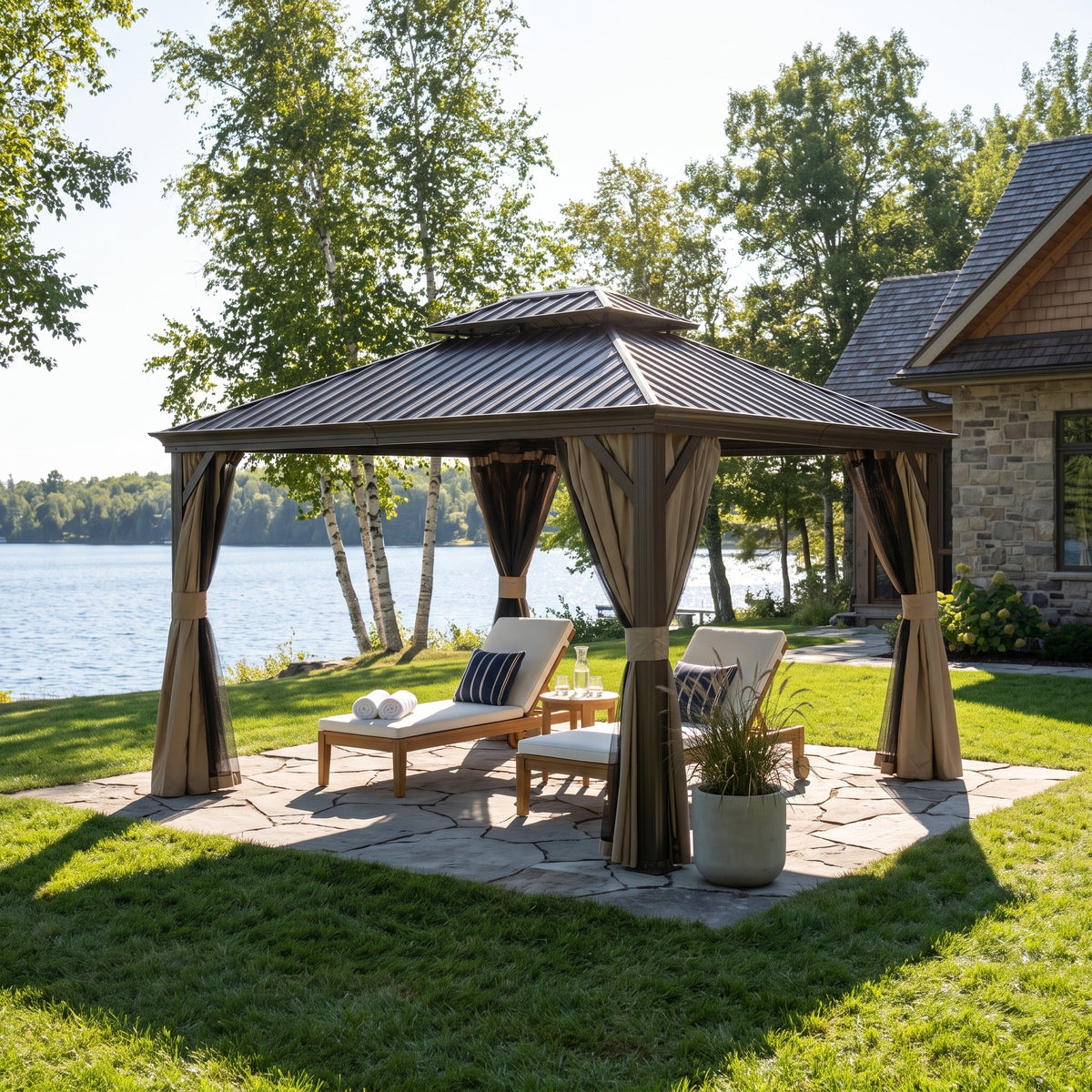 Brown aluminum 12x14 double roof hardtop gazebo with tan curtains over two lounge chairs on a stone patio by a lake