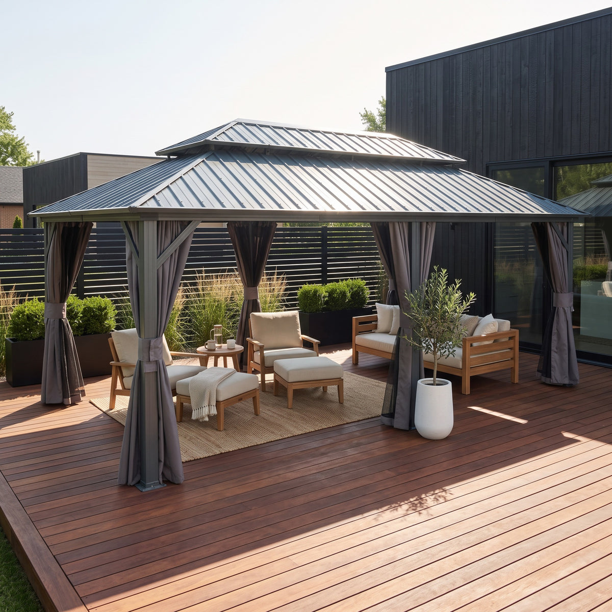 Gray aluminum 12x20 double roof hardtop gazebo with tied curtains over teak lounge chairs on a wood deck