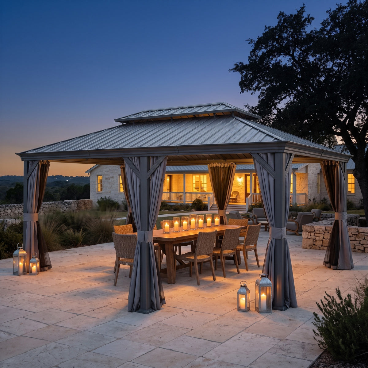 Gray 14x22 hardtop gazebo with tied back curtains over a candlelit dining table on a stone patio at dusk