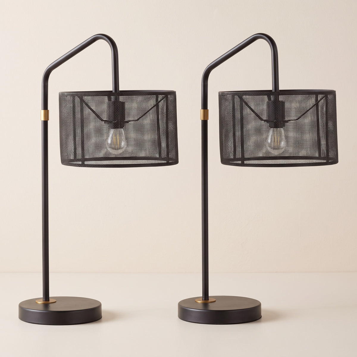 Set of two black metal mesh shade table lamps with gold accents on an ivory backdrop