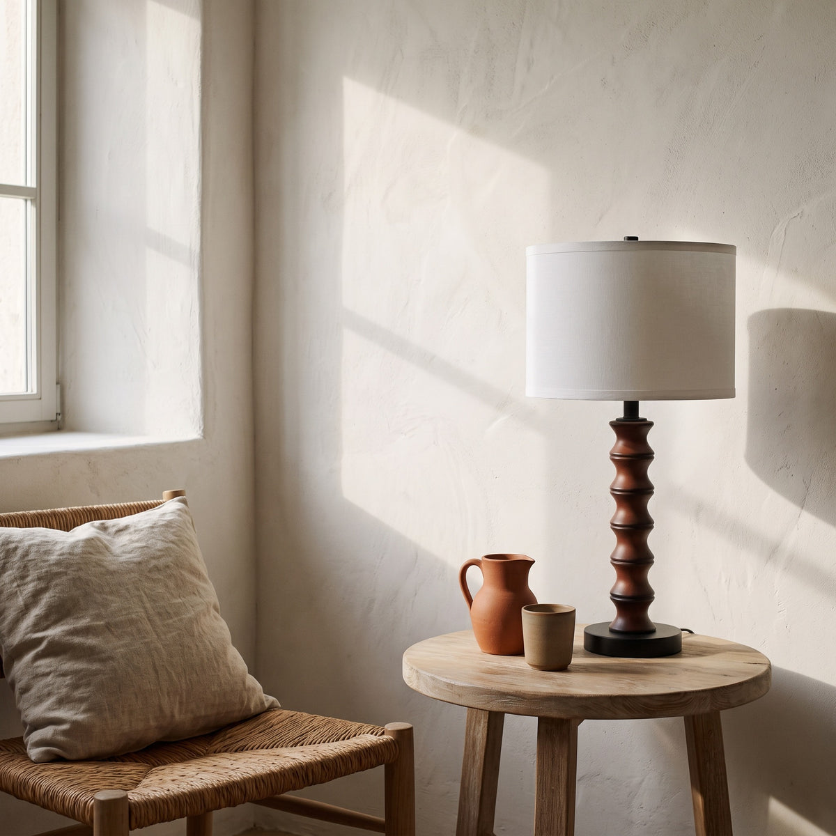 Cherry turned table lamp with white linen-look drum shade on an oak side table beside a sunlit window