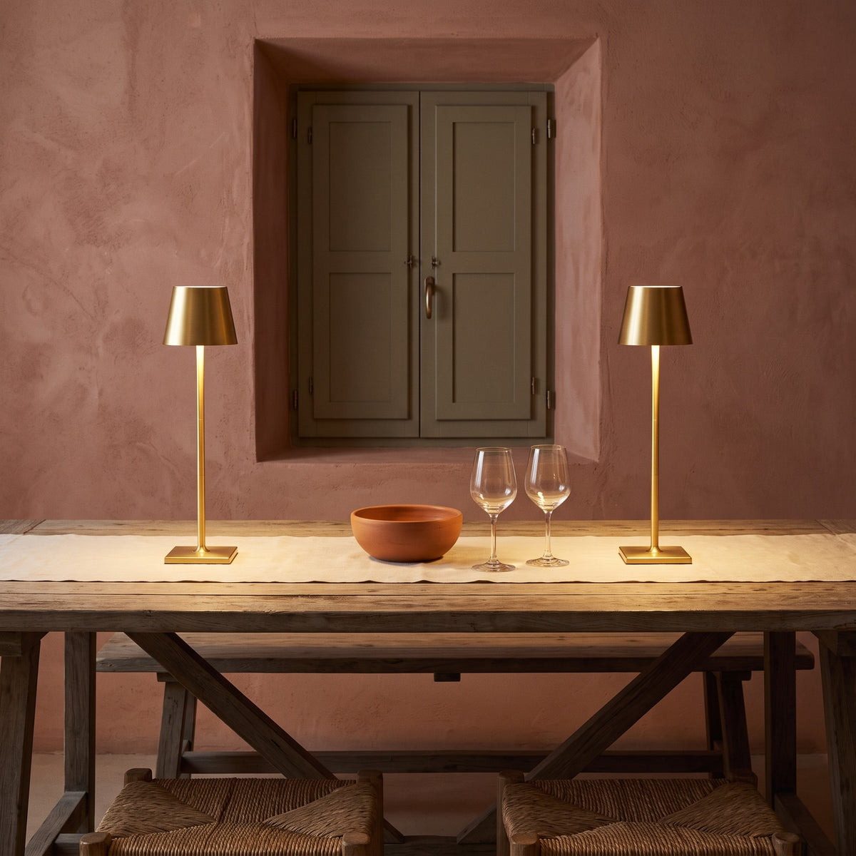 Pair of gold cordless table lamps glowing on a linen runner over a rustic wood dining table