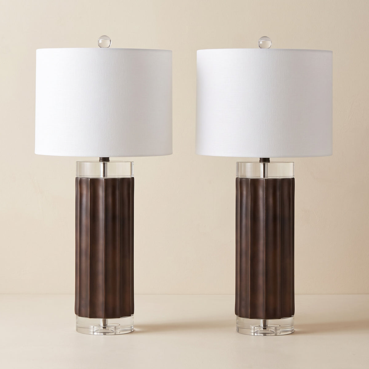Pair of brown fluted table lamps with clear crystal bases and white linen drum shades on an ivory backdrop
