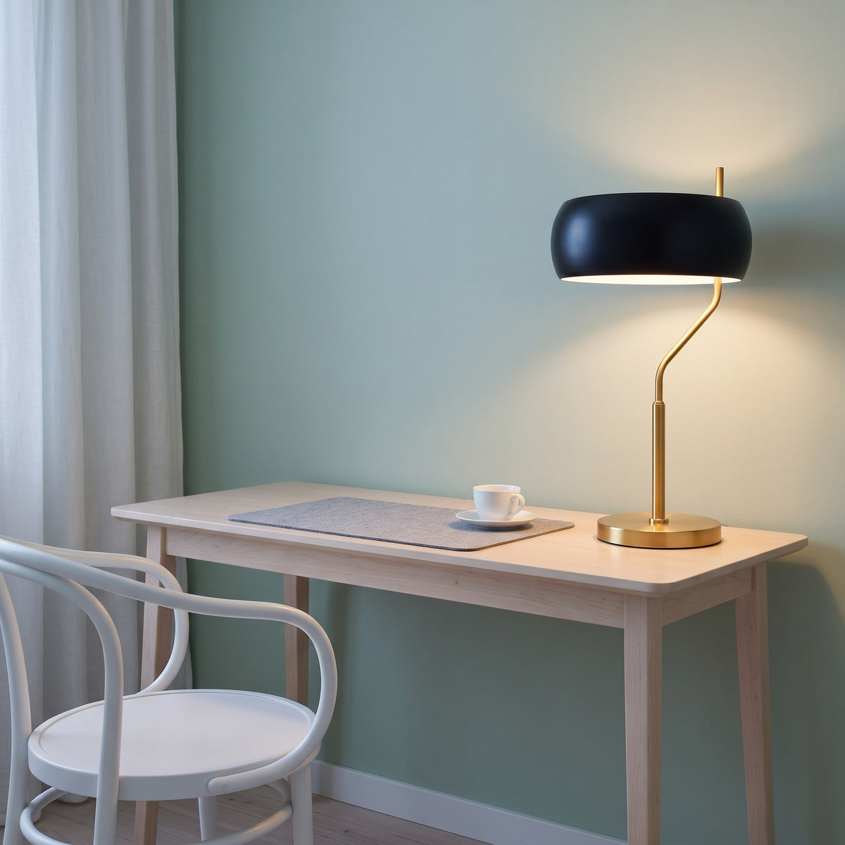 Gold and black table lamp with a domed metal shade, lit on a light wood desk against a sage green wall