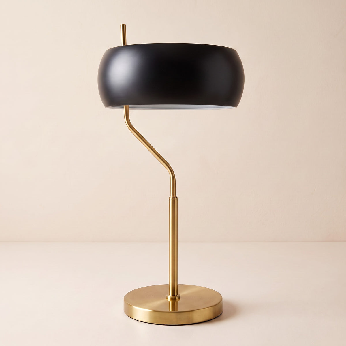 Black dome shade table lamp with brushed gold offset stem and round base on an ivory backdrop