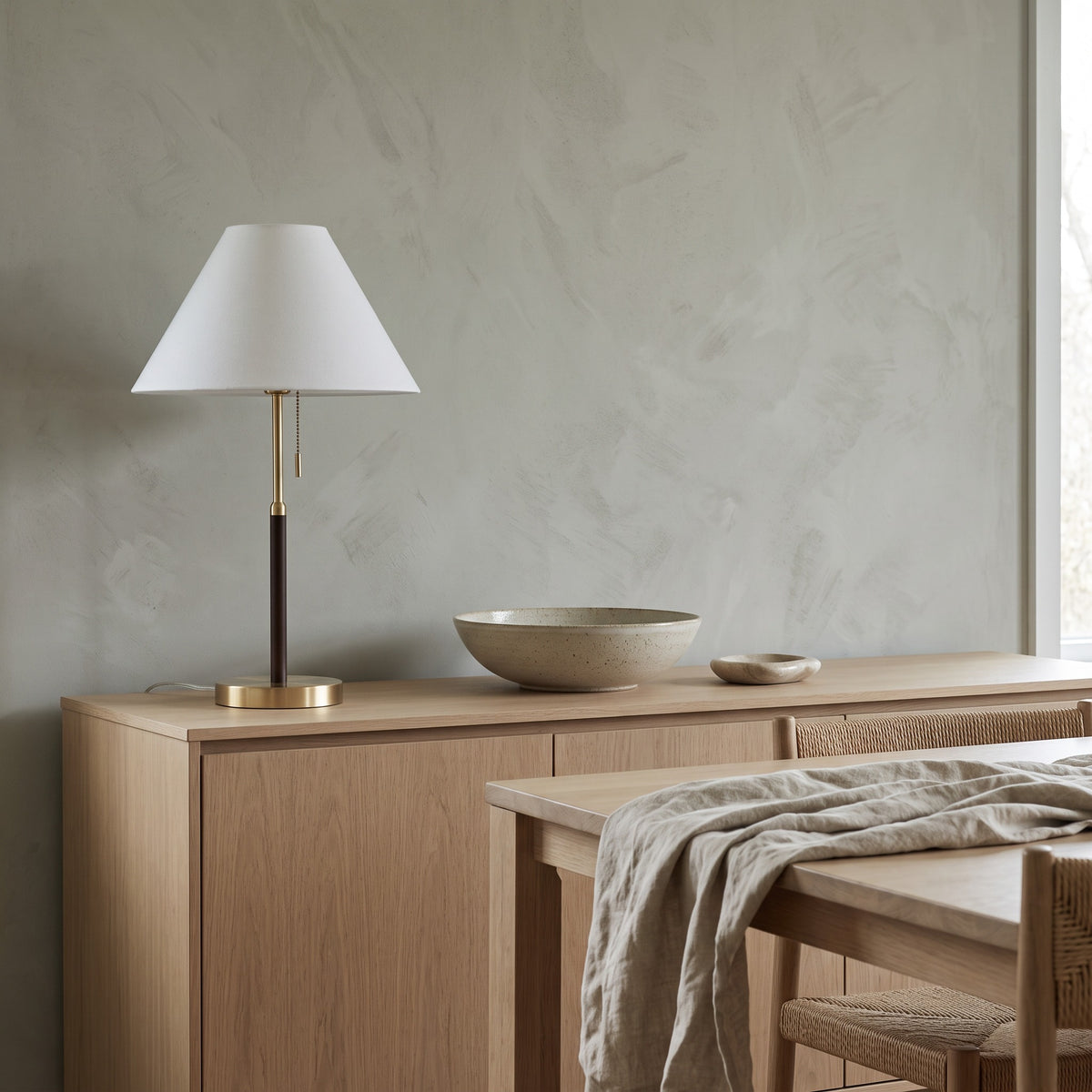 Table lamp with white fabric shade, brass and dark brown stem and gold base on an oak sideboard in a dining room