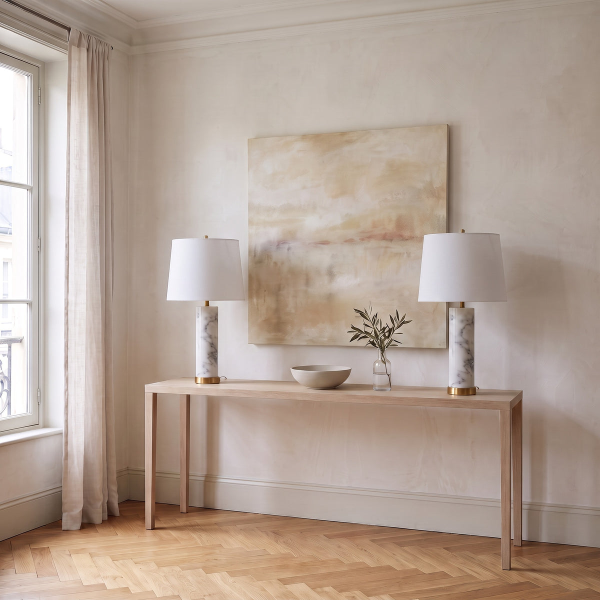 Pair of white marble table lamps with white linen shades and brass bases on a light oak console