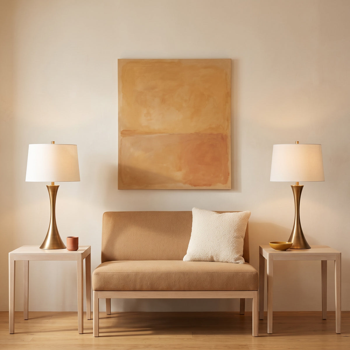 Pair of bronze hourglass table lamps with white linen drum shades on oak side tables beside a camel settee
