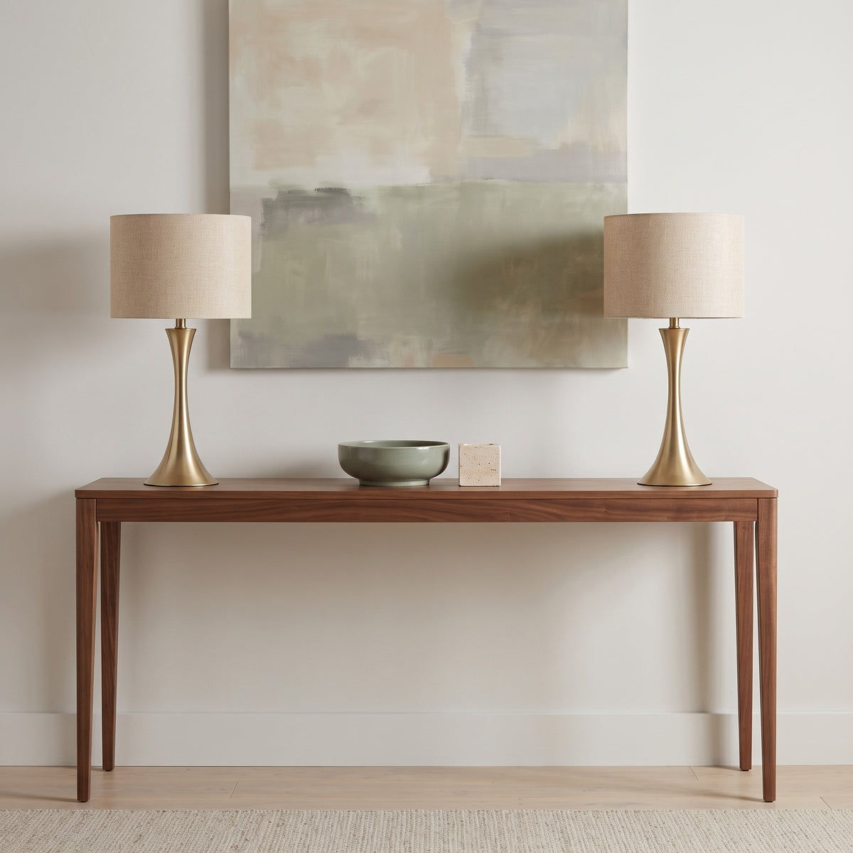 Pair of gold table lamps with beige linen drum shades on a walnut console below an abstract canvas