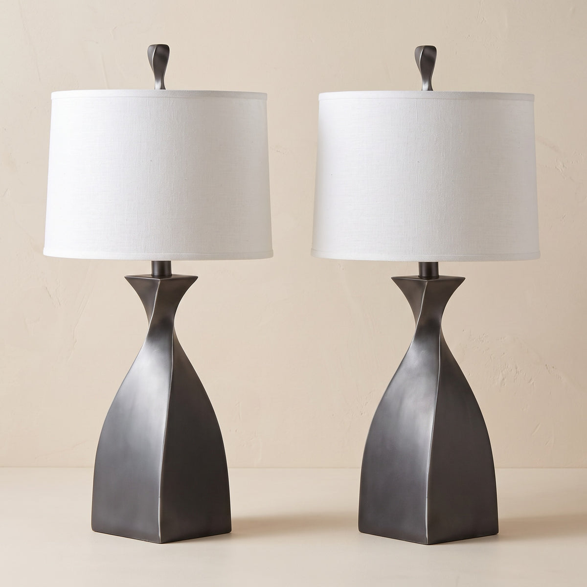 Pair of grey twisted base table lamps with white linen drum shades on an ivory plaster backdrop