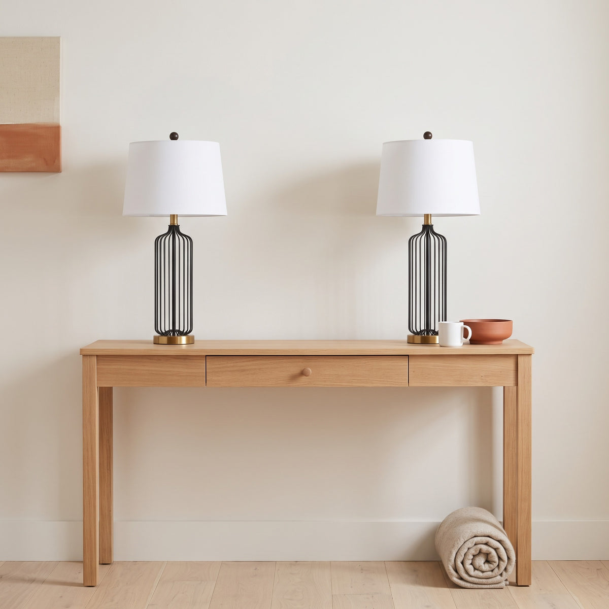 Pair of black wire cage table lamps with brass bases and white drum shades on an oak console table