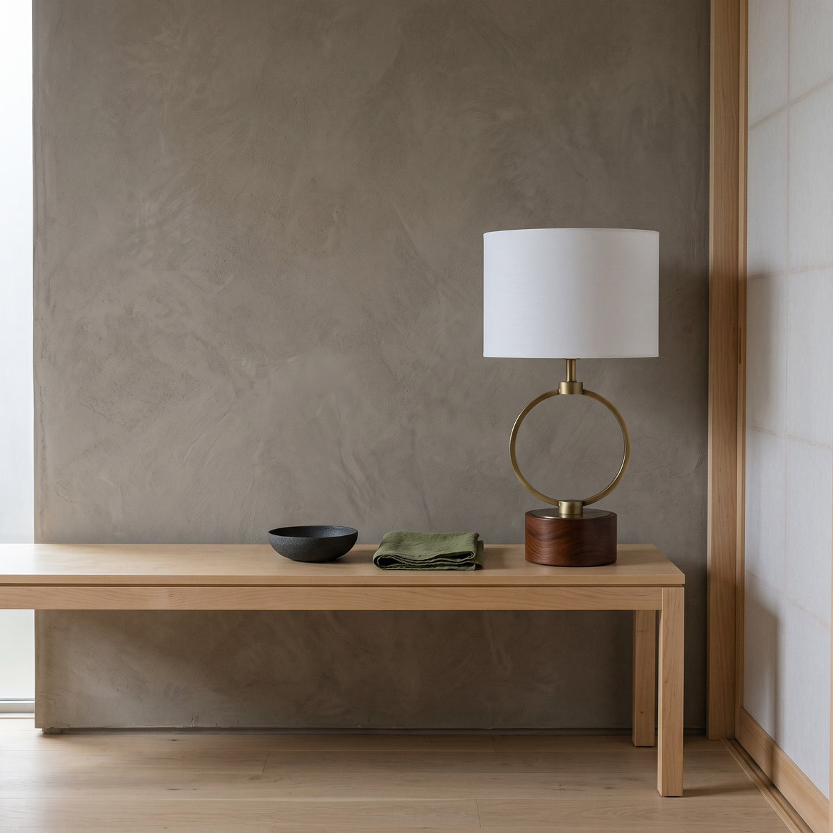 Table lamp with white linen shade, bronze finish ring and walnut finish wood base on a light wood bench