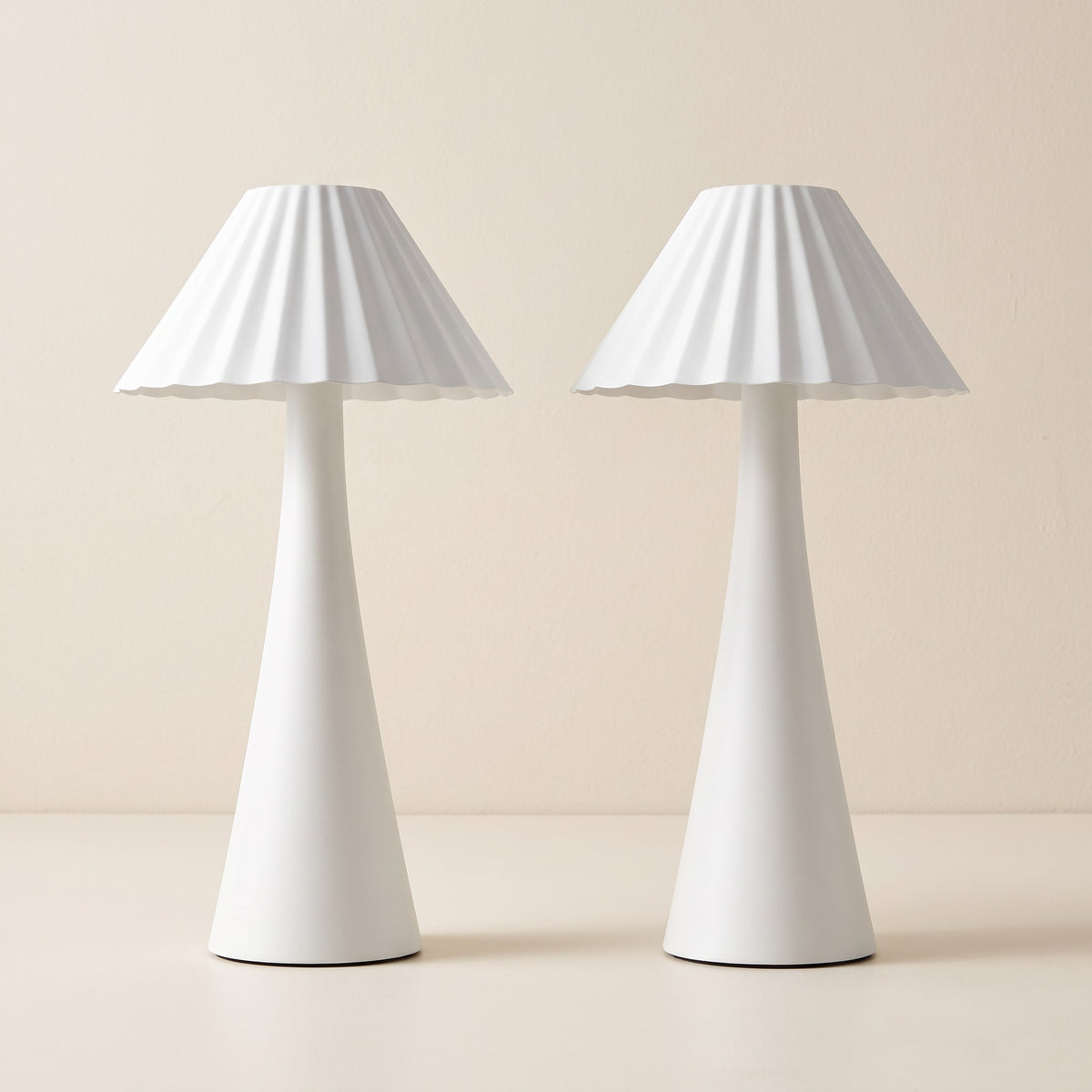 Two white pleated metal table lamps with scalloped cone shades on an ivory plaster backdrop
