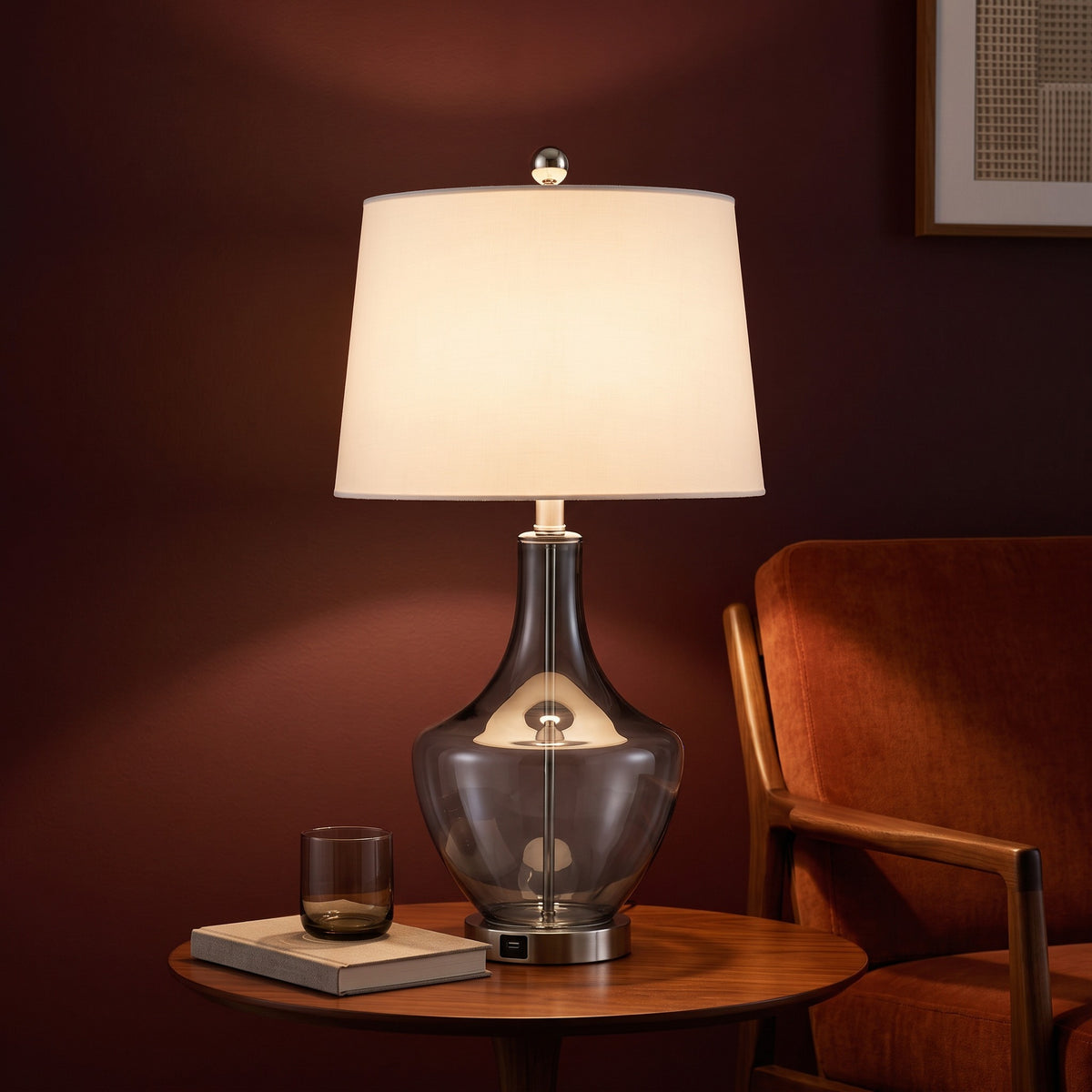 Grey glass table lamp with white fabric shade and USB port base, lit on a walnut side table beside a rust lounge chair