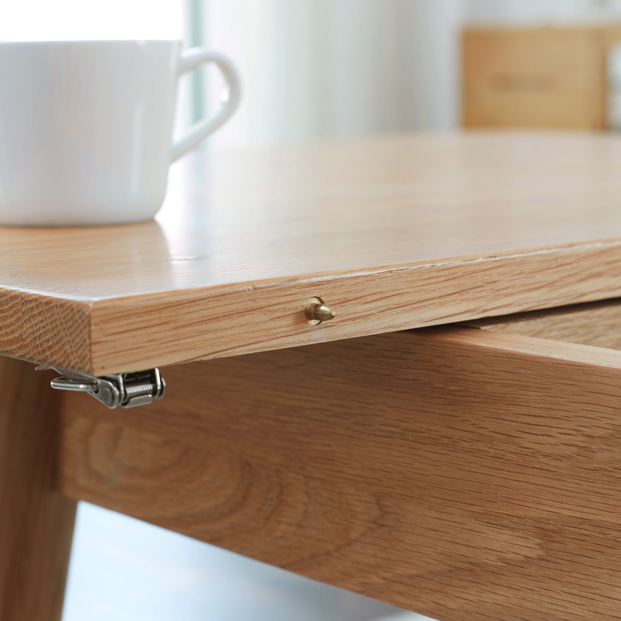 Close-up of the oak table edge with a brass alignment pin and spring latch beneath