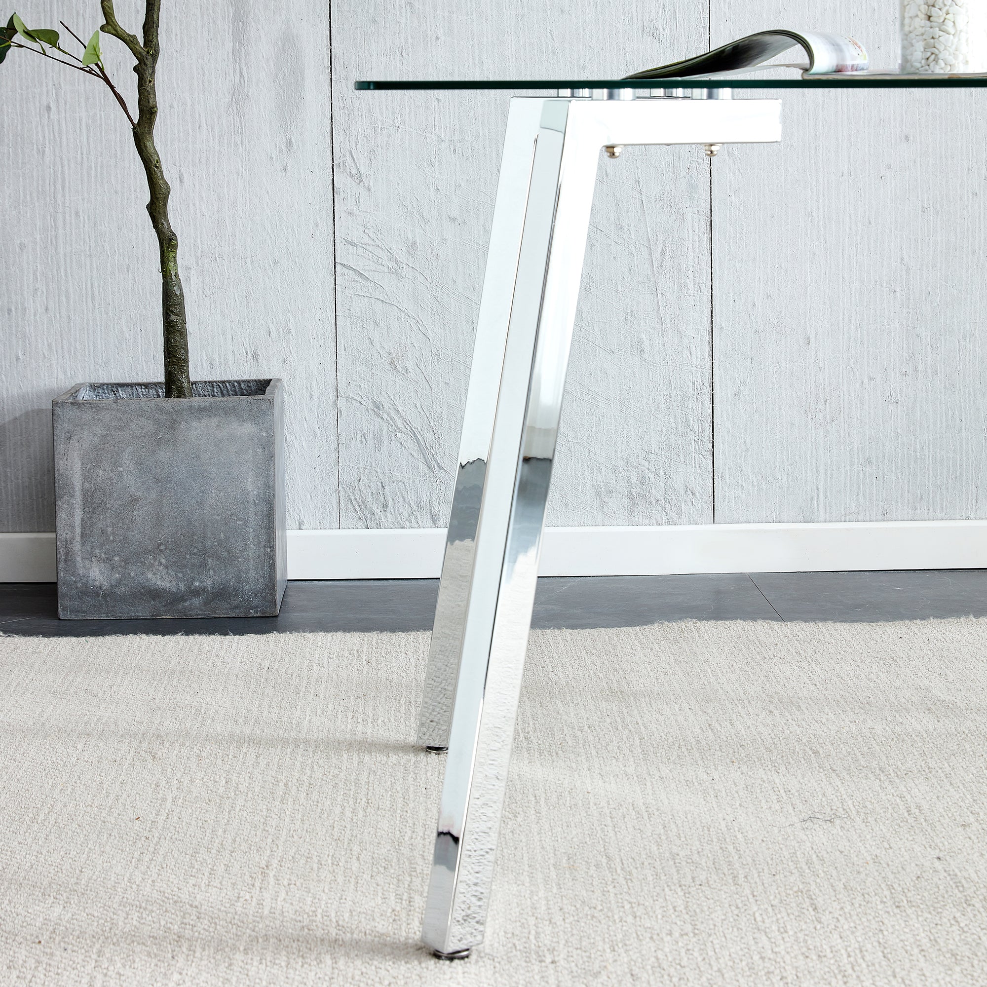 Close-up of an angled chrome leg joining the glass tabletop beside a potted plant