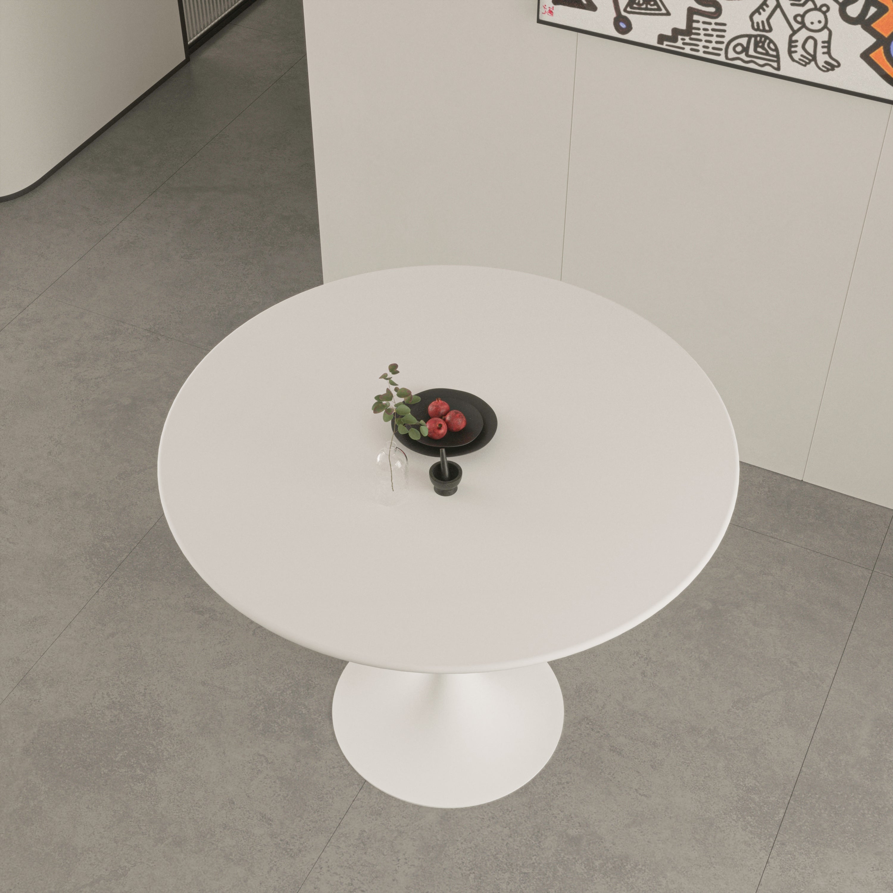 Overhead view of white round tulip dining table with a black plate of pomegranates on gray tile