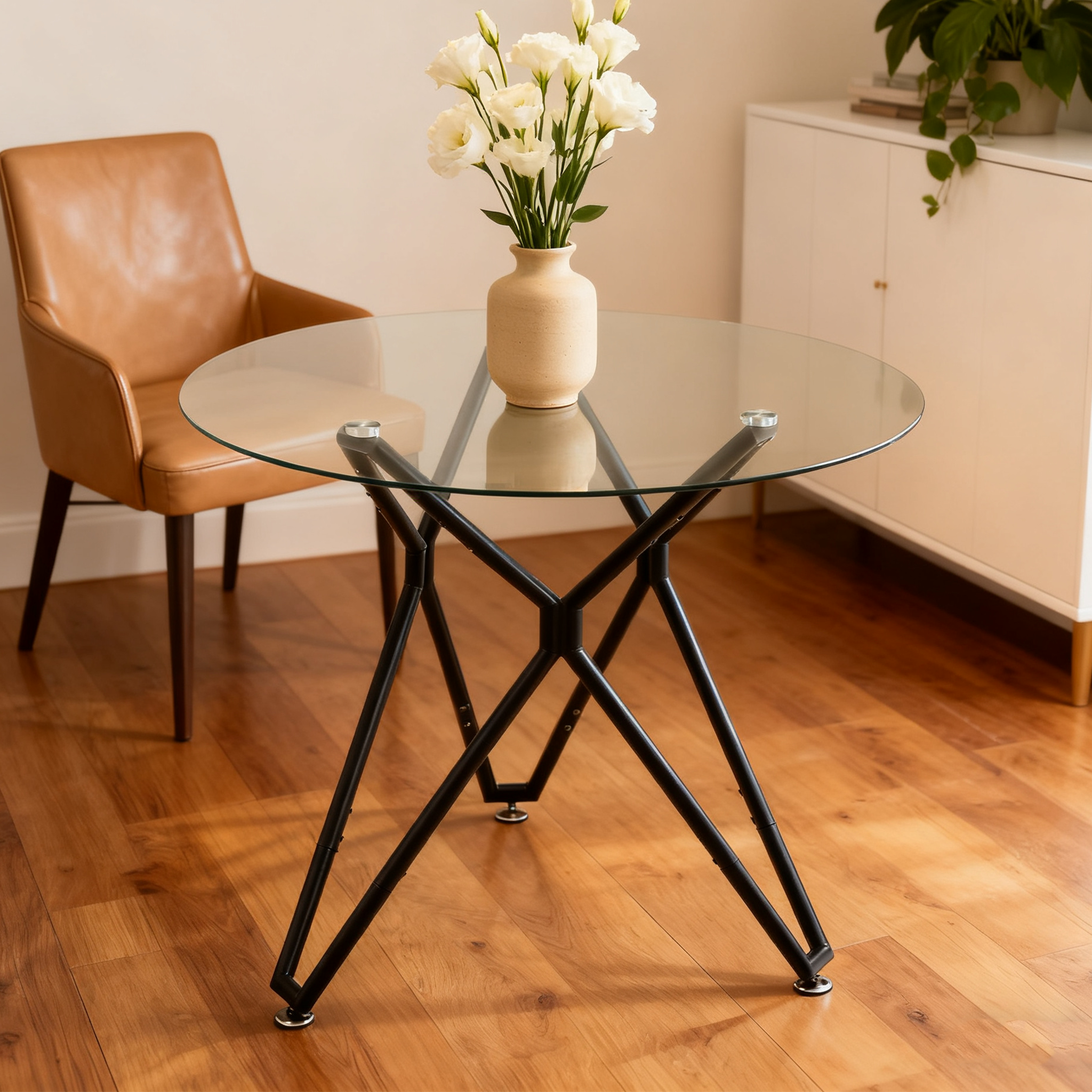 Round glass dining table with a black base and a tan leather chair, ceramic vase of white flowers on top