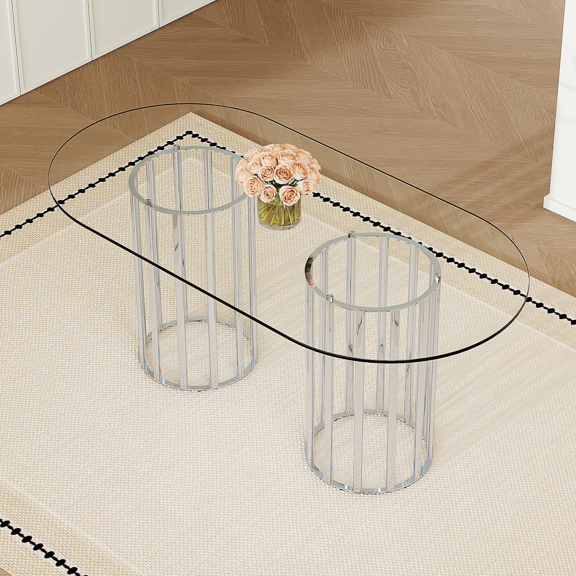 High angle view of the oval glass dining table with two silver column pedestals over a patterned rug.