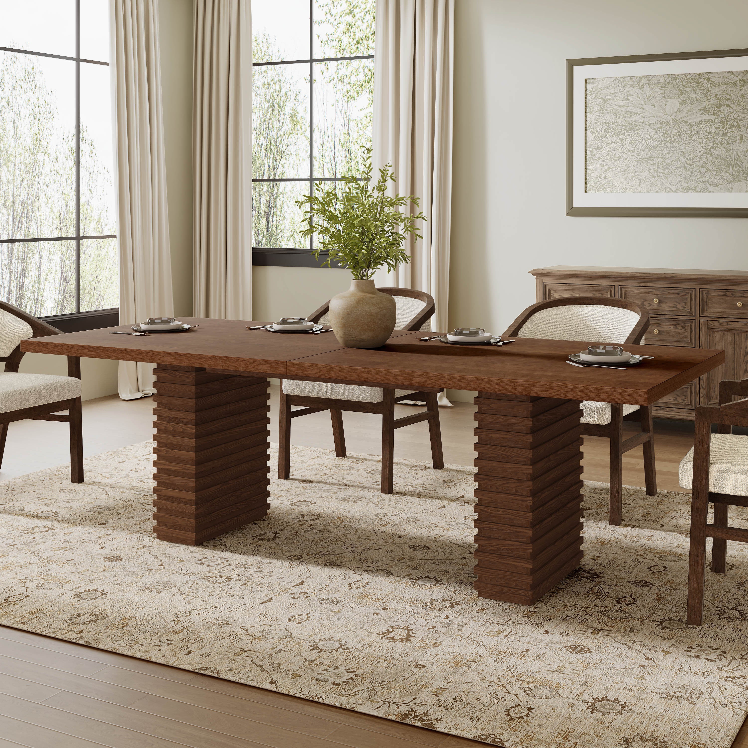 Walnut double-pedestal dining table set with plates and a vase in a sunlit dining room with boucle chairs