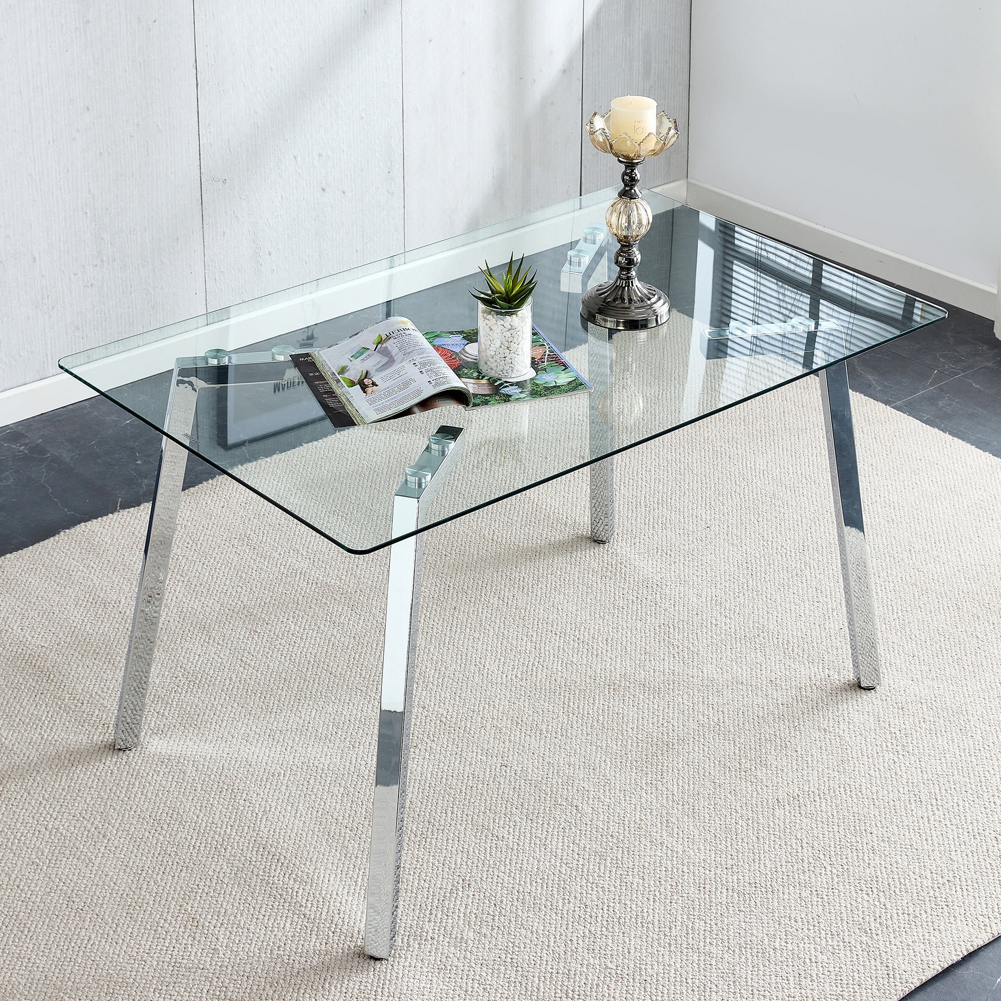 Rectangular glass dining table with angled chrome legs styled overhead with a magazine, plant and candle holder