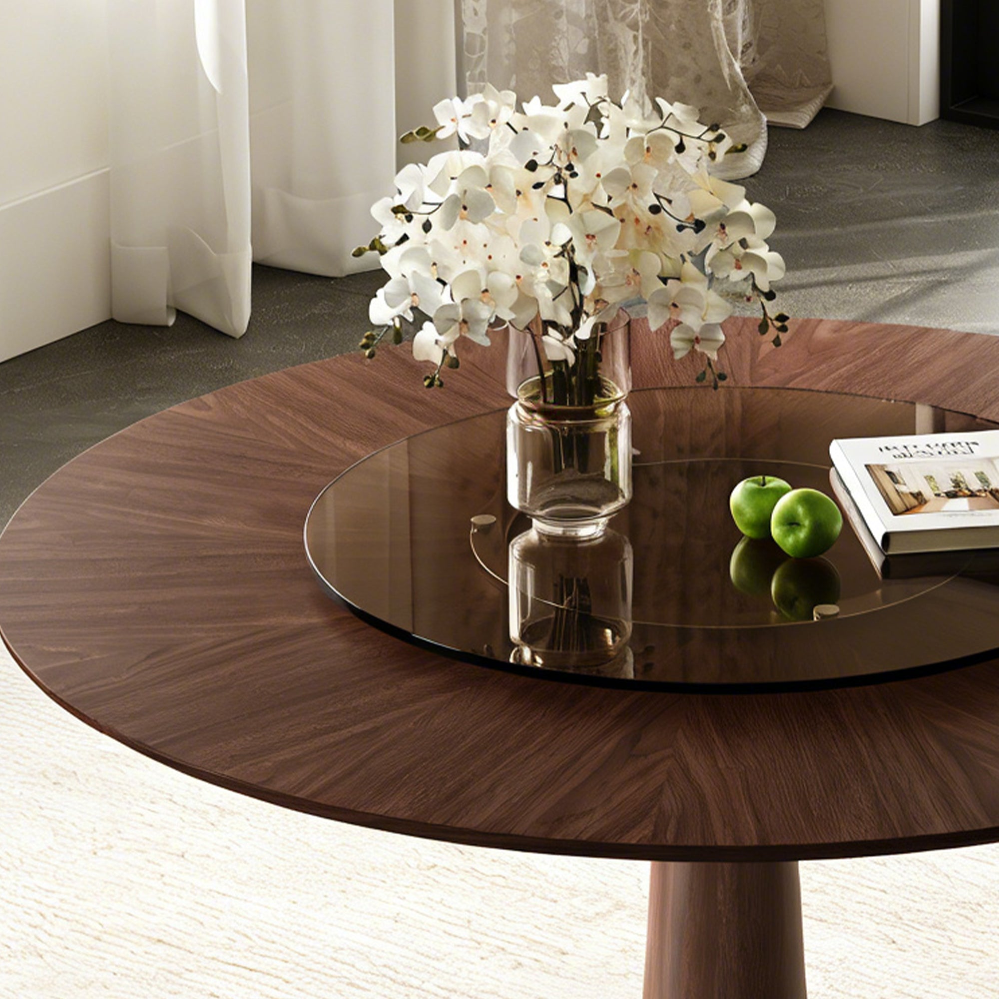 Close-up of the walnut tabletop and brown glass turntable holding orchids, apples and a book