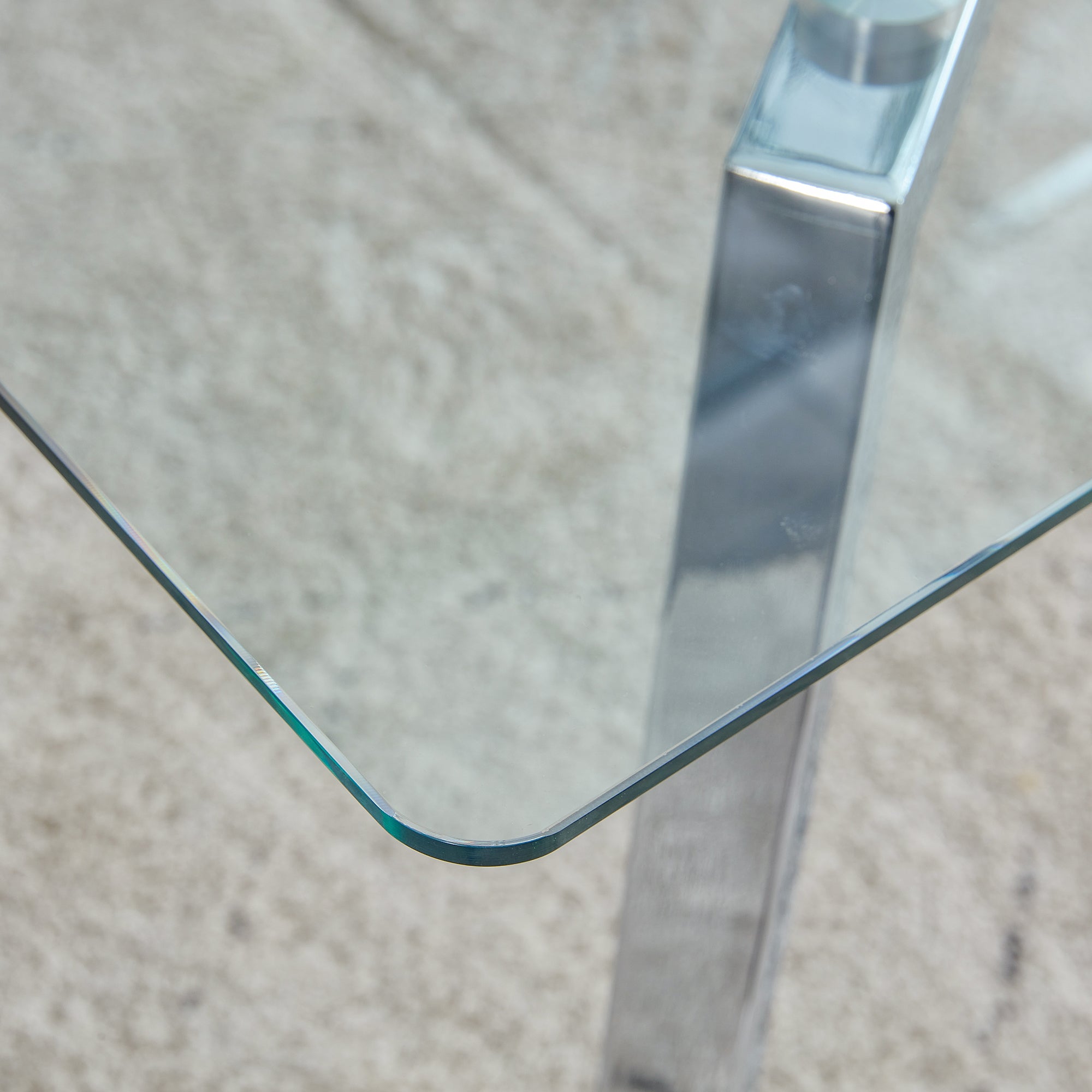 Close-up of the rounded glass corner and polished chrome leg on carpet