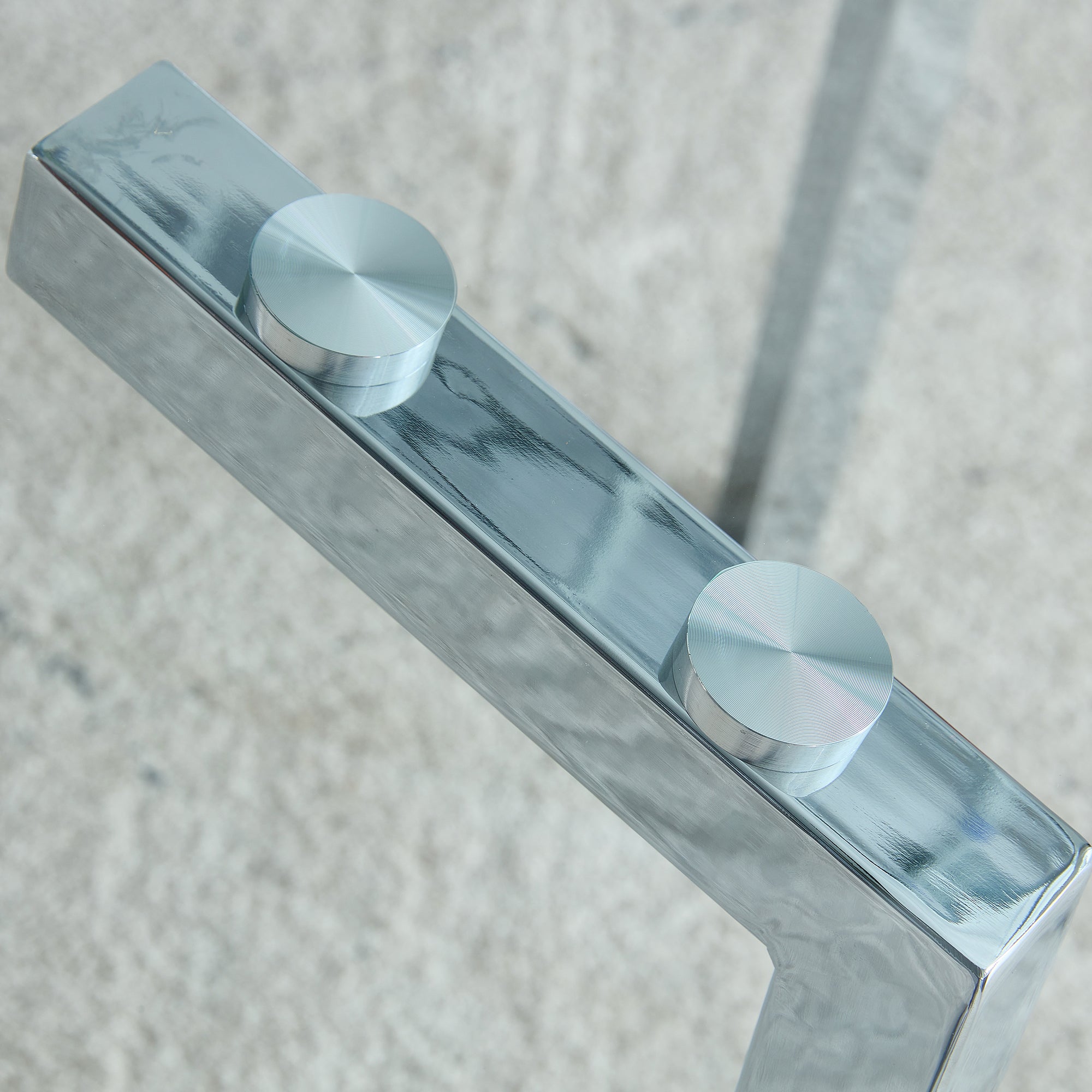 Studio close-up of a chrome leg bracket with two silver bolt caps fastening the glass top