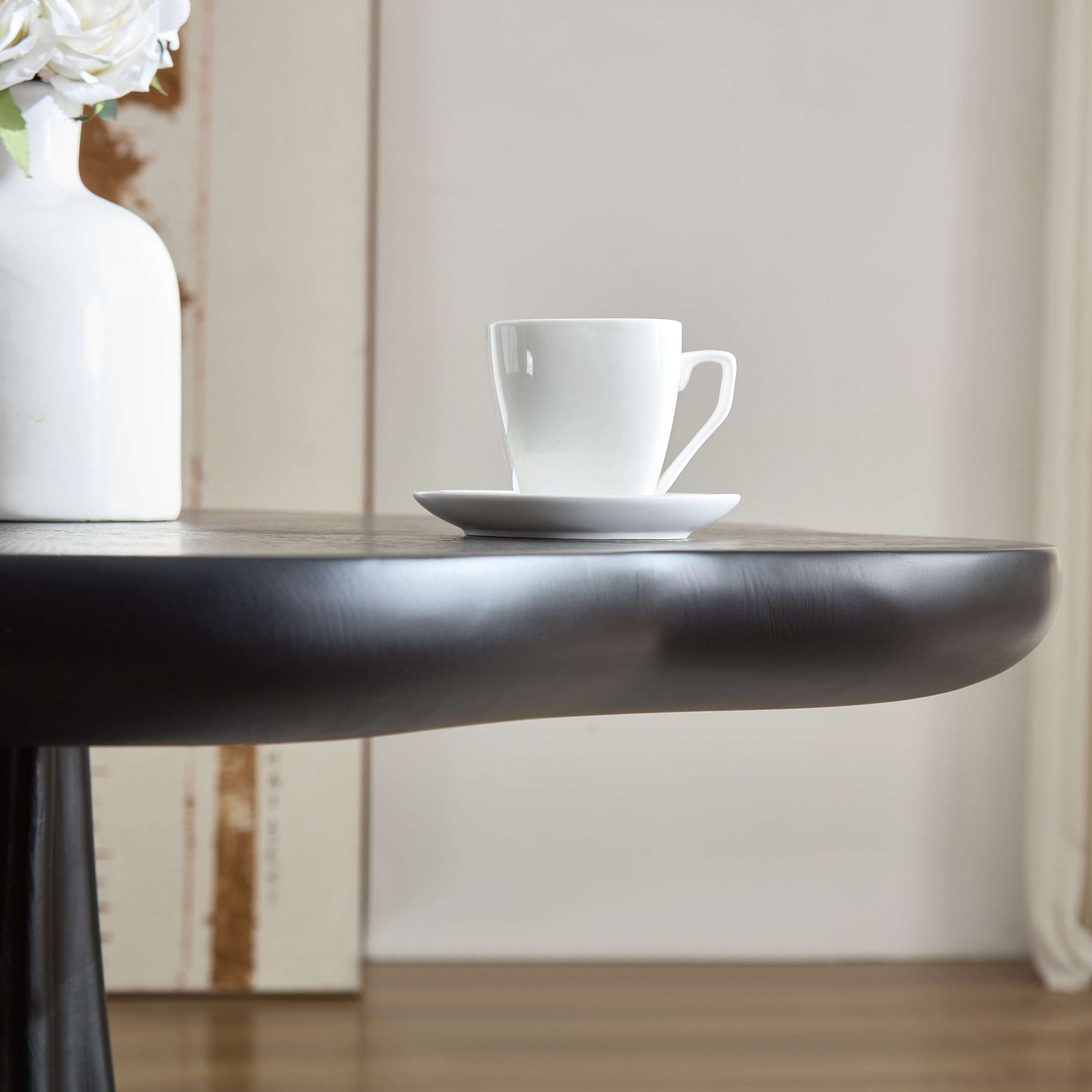 Styled close-up of the black petal tabletop edge with a white cup and vase
