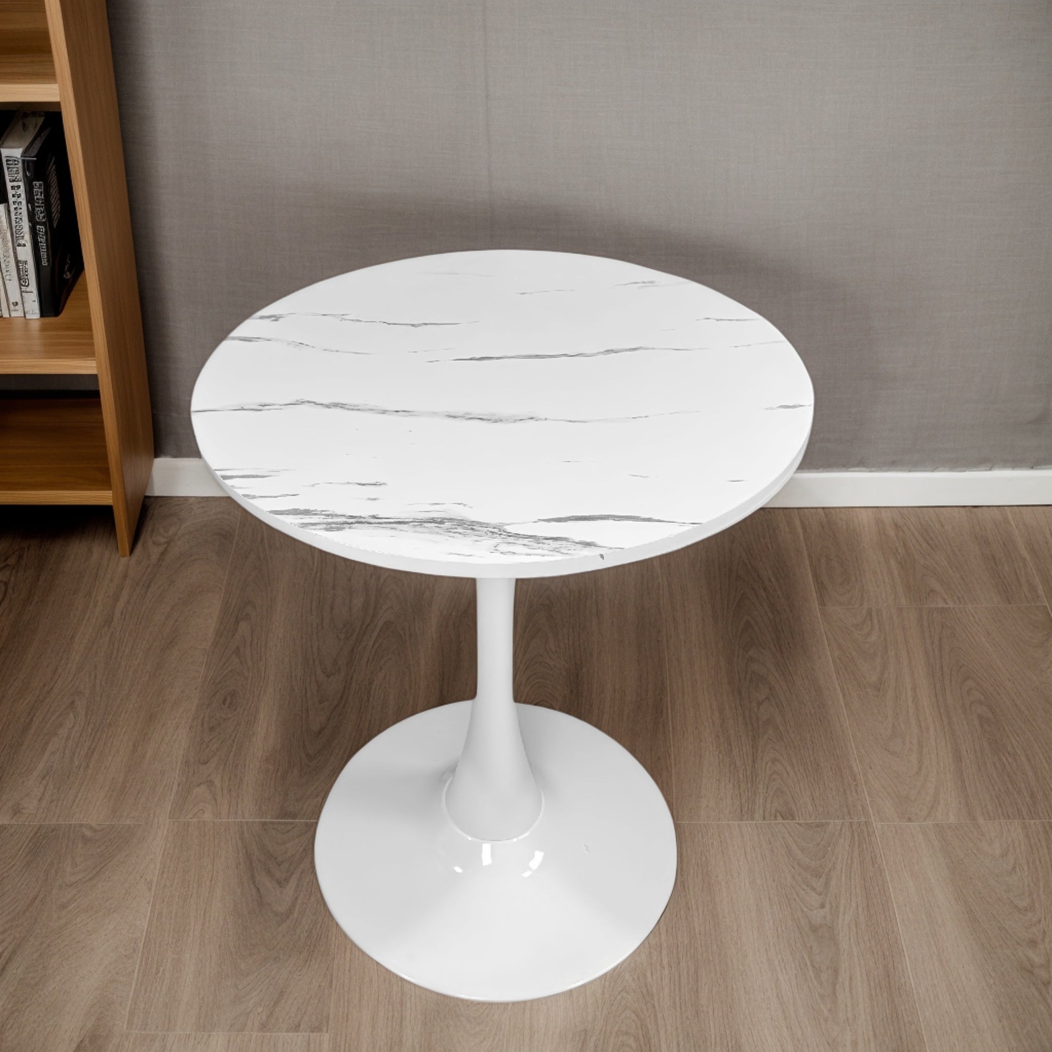White marble tulip bistro table on wood flooring beside a bookshelf, three-quarter view