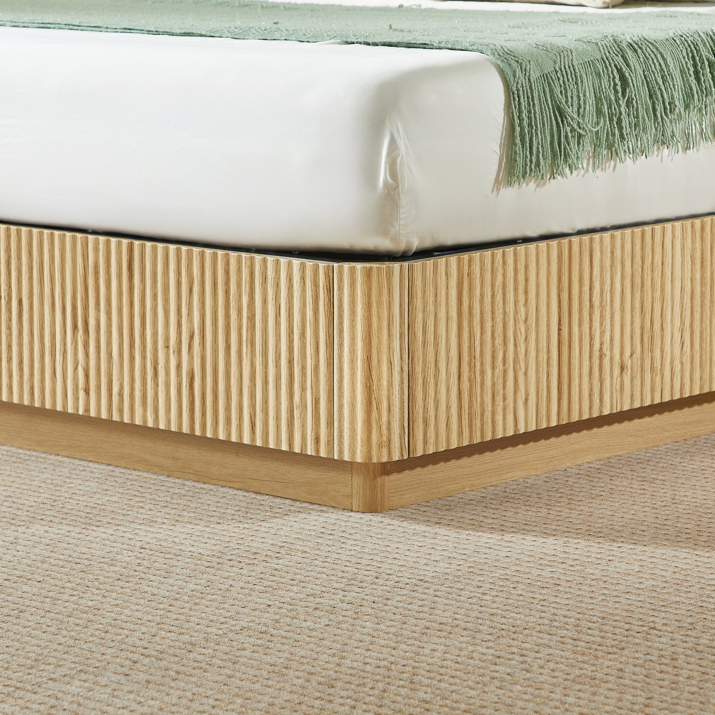 Closeup of the light oak fluted base corner and mattress edge with green fringed throw #Color_Oak