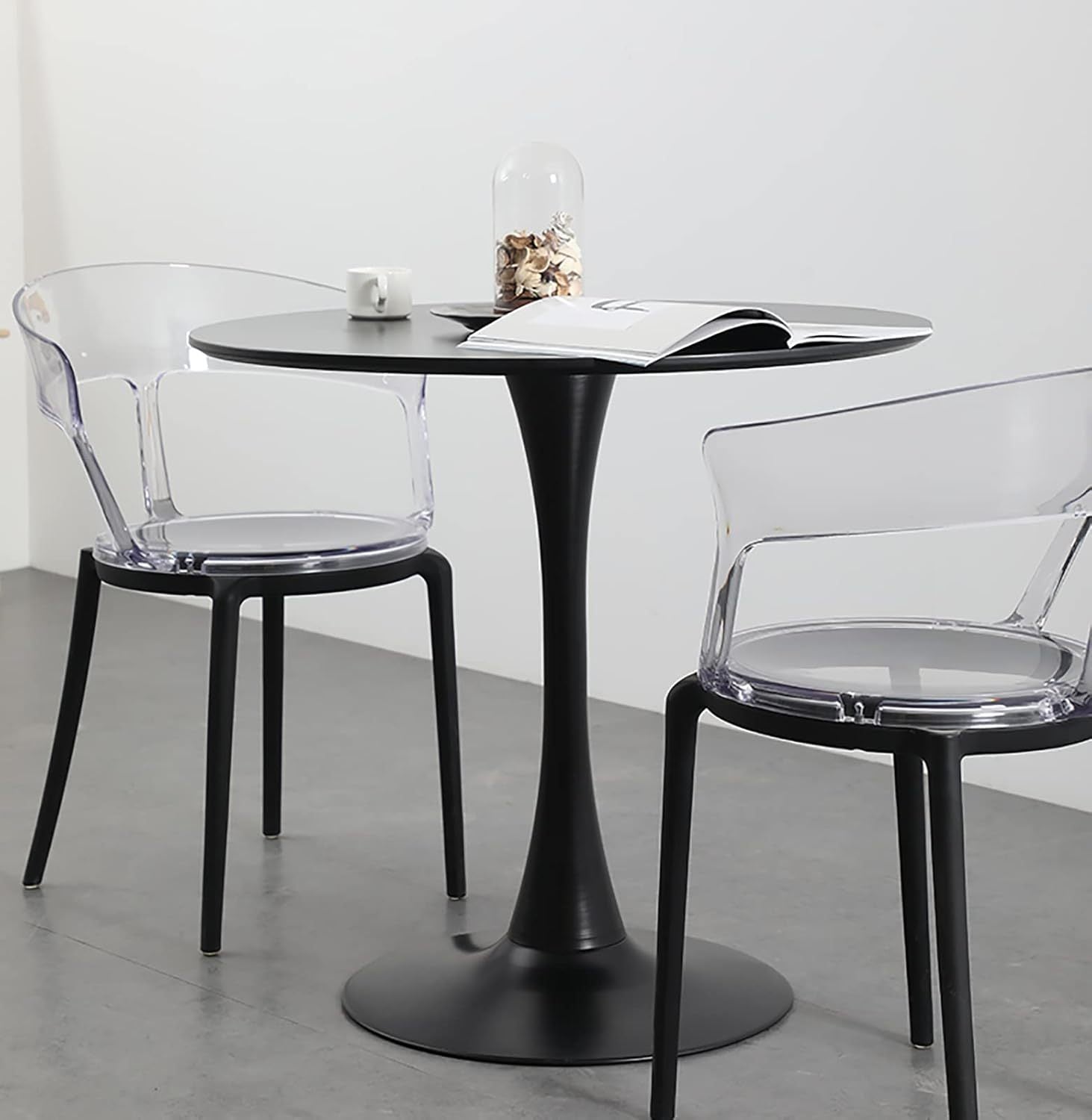 Round black tulip table with two clear armchairs, a mug and an open book