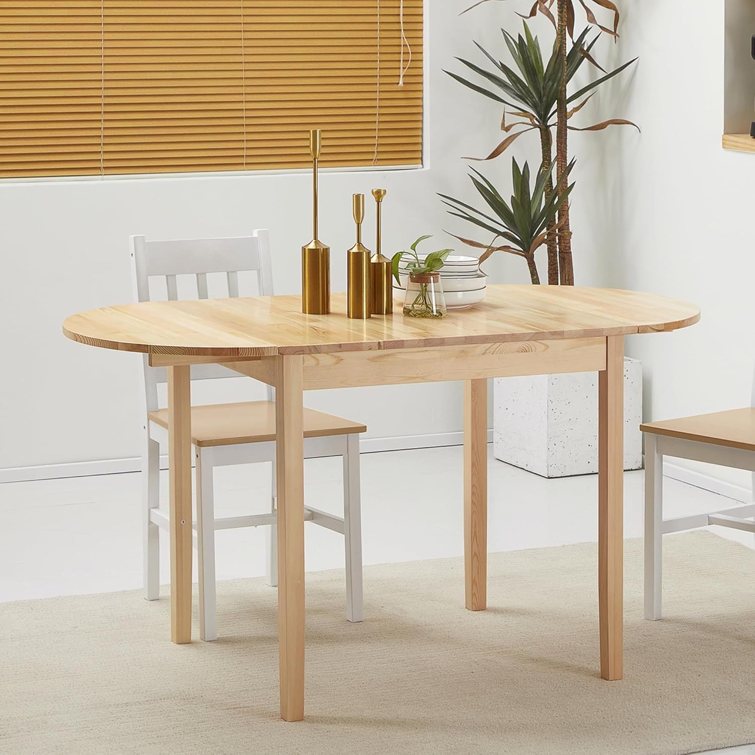 Side view of the natural pine drop-leaf dining table with white chairs in a bright room