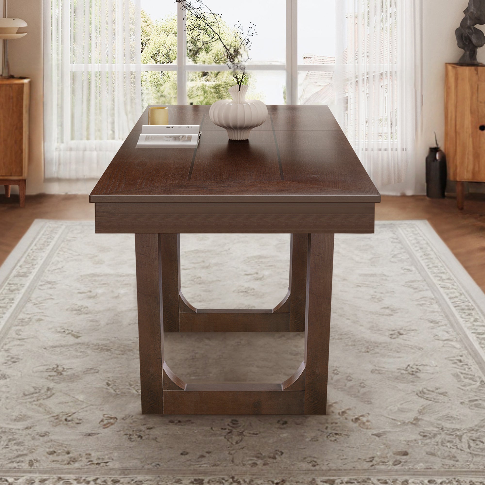 Angled end view of the walnut farmhouse dining table beside a large window in a styled room