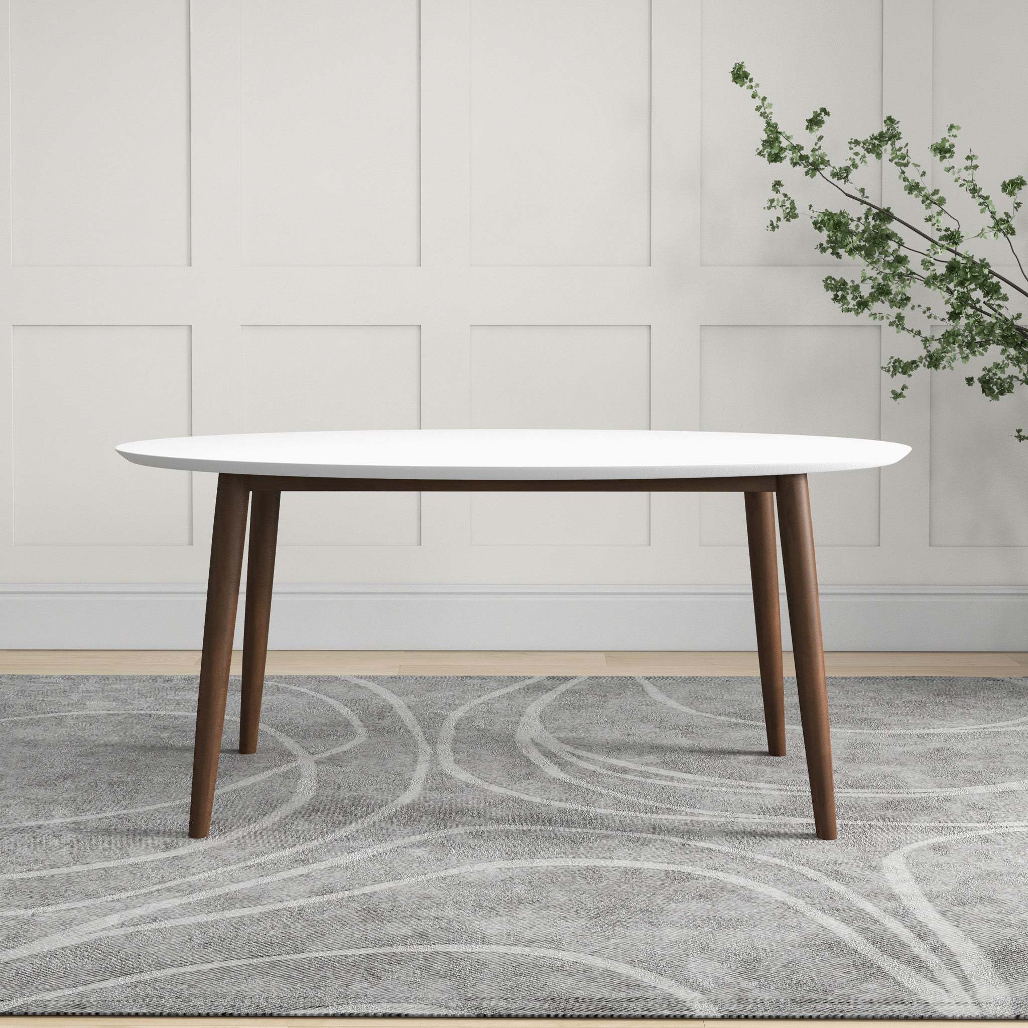 White oval dining table styled against a paneled wall with a leafy branch