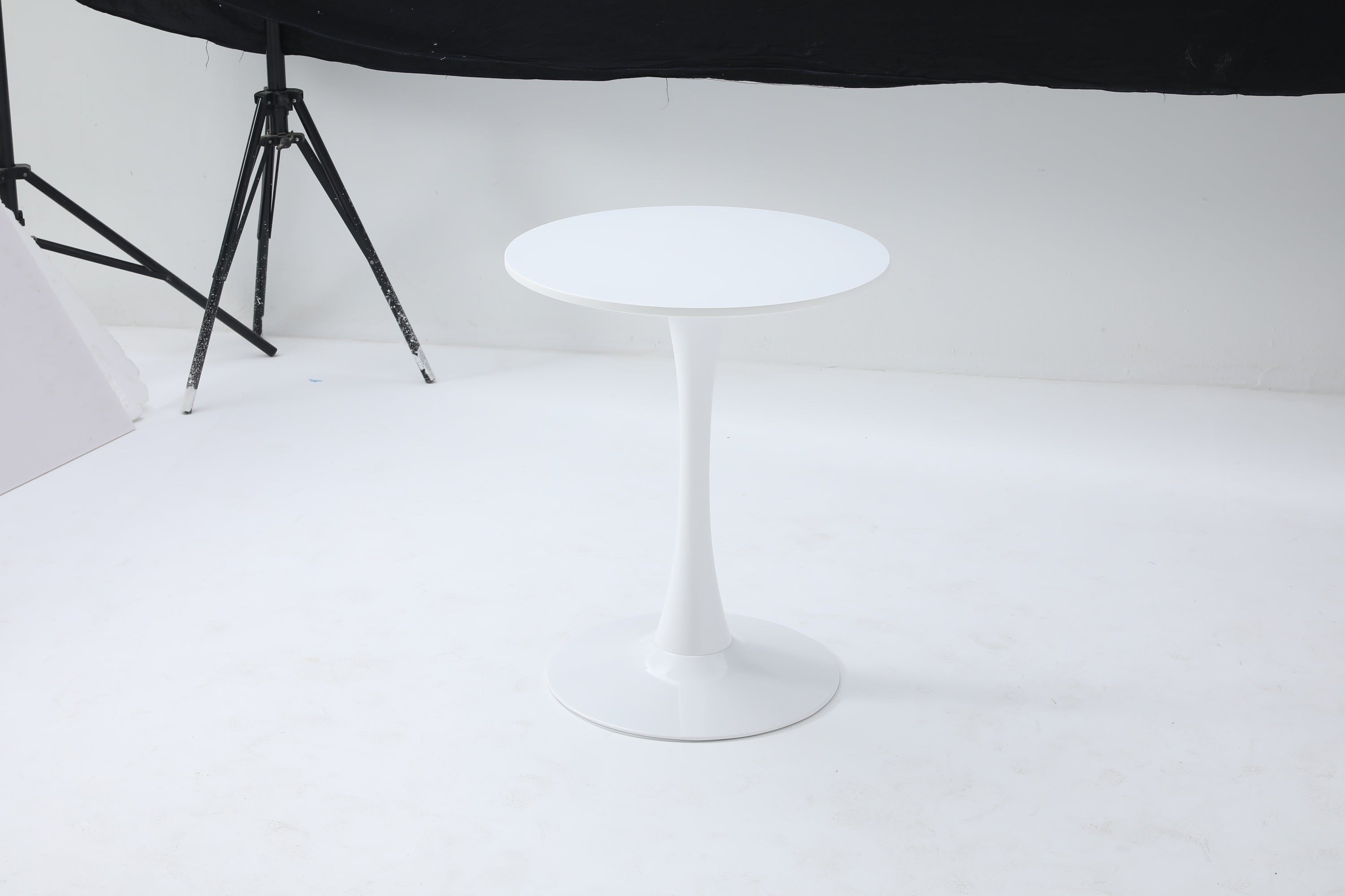 White round tulip bistro table alone in a photo studio with backdrop and tripod visible