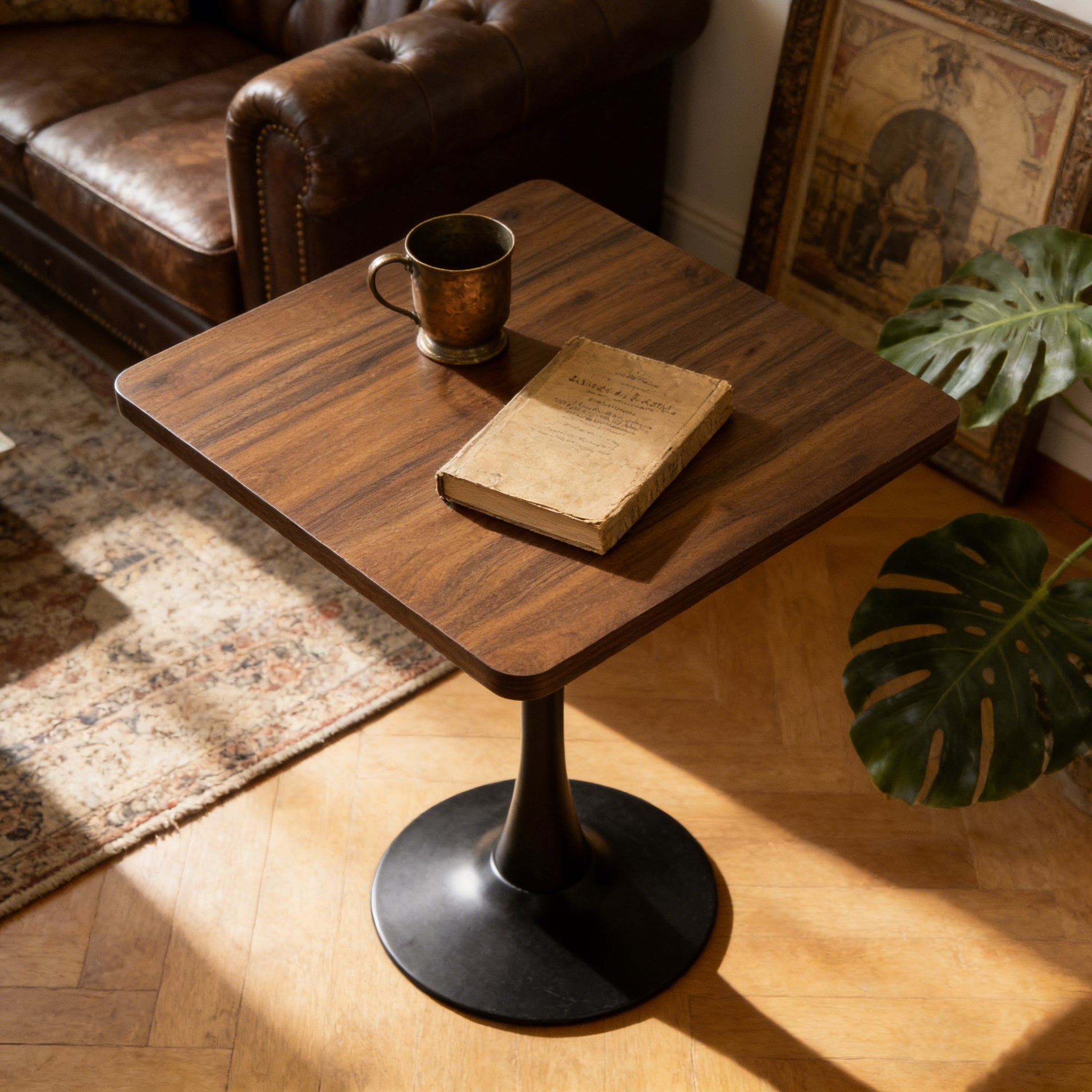 Walnut square tulip table beside a leather sofa with a brass mug and worn book in warm light