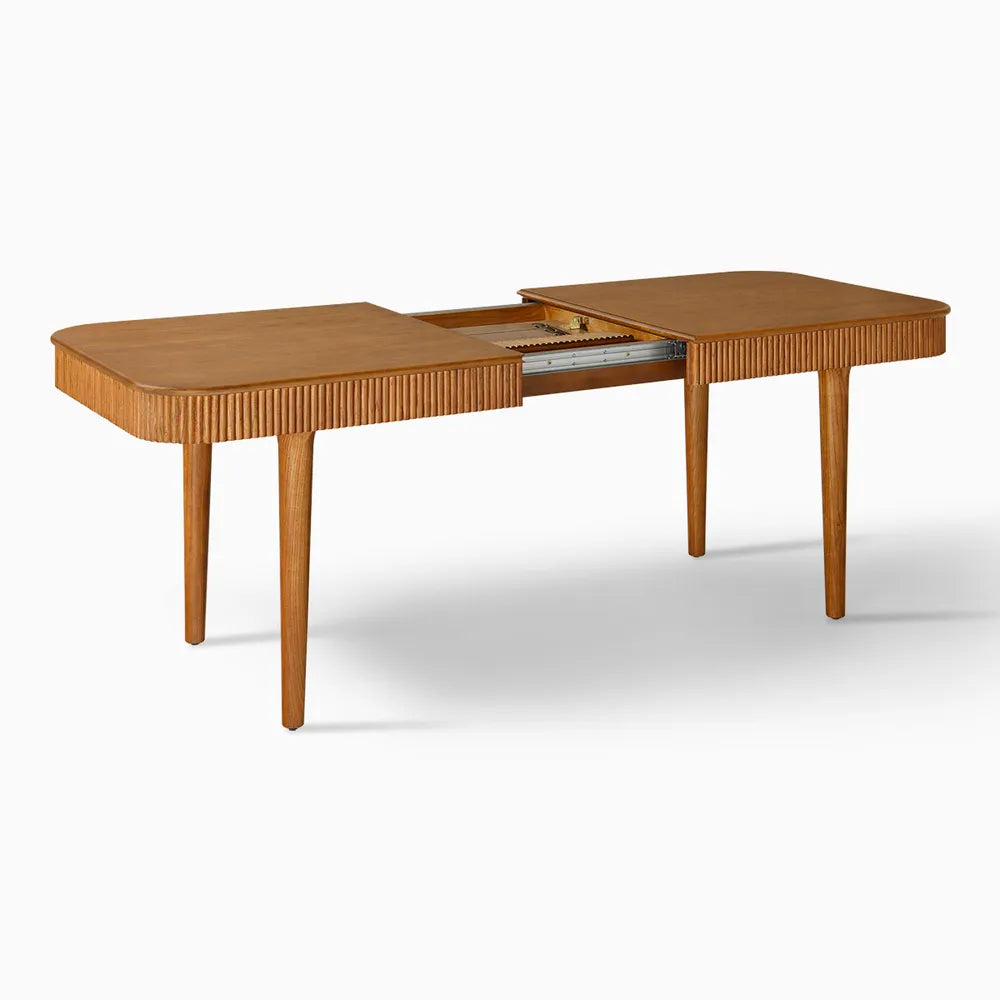 Shot of ash wood dining table partially extended, revealing interior extension mechanism and fluted detailing in a mid-century modern design.