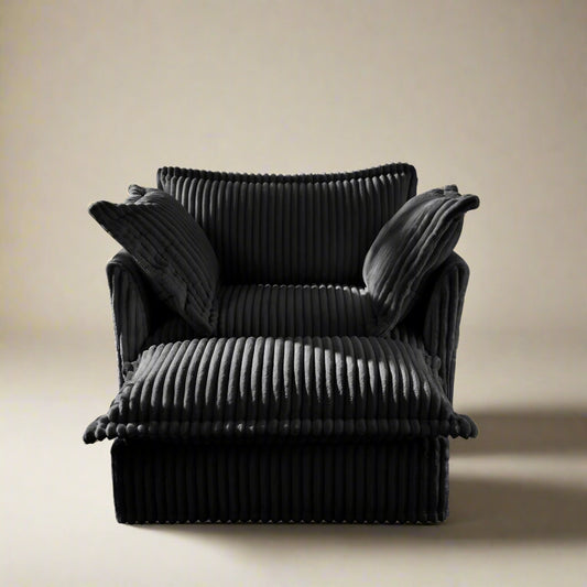 studio shot of the fluffy chair sofa in black corduroy with an ottoman showing the plush texture and two pillows and details of the couch