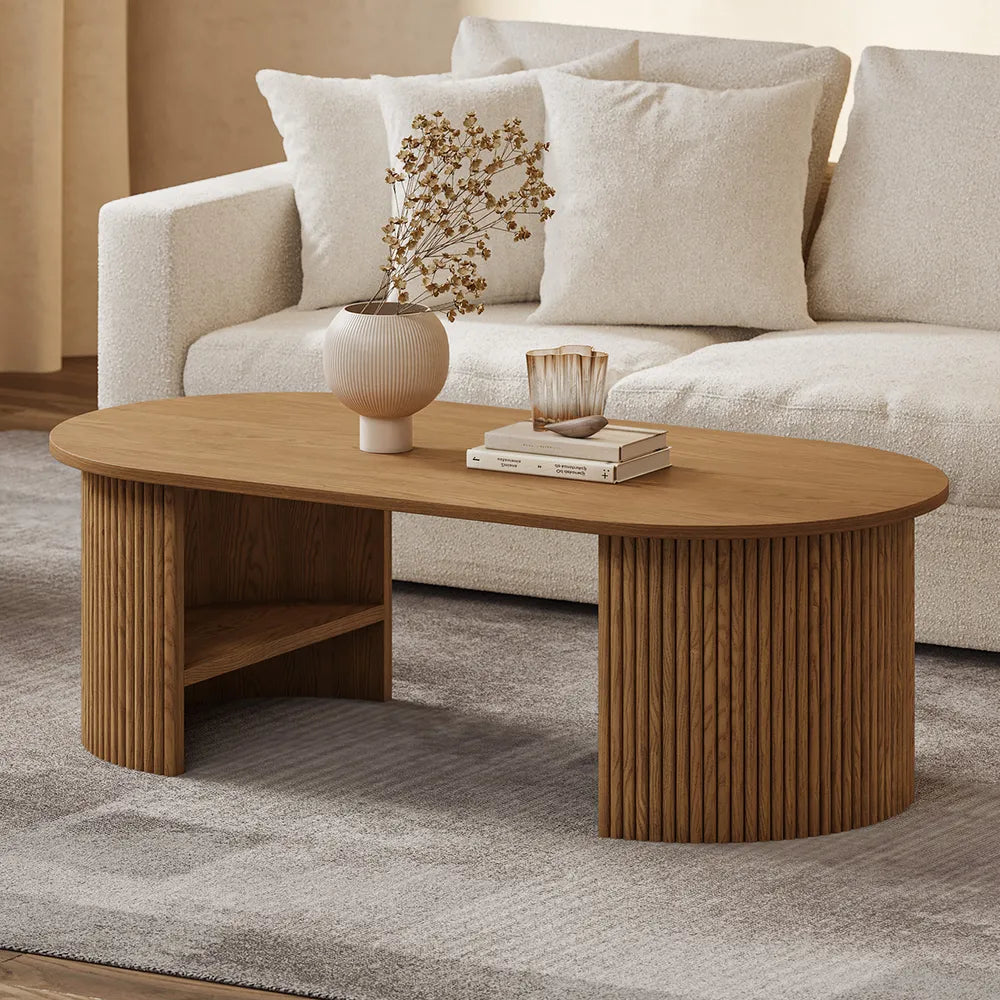 Oval coffee table with fluted wood legs styled in a neutral living room, topped with books and decor for a warm, modern look.