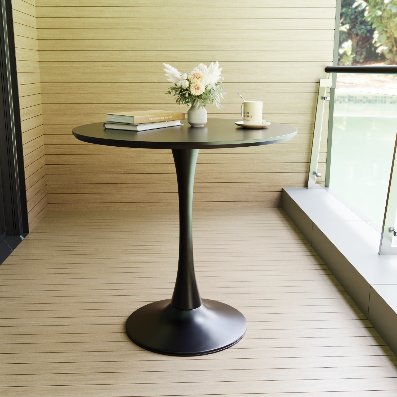 Black tulip dining table on a wood deck beside a glass railing, styled with books and a vase