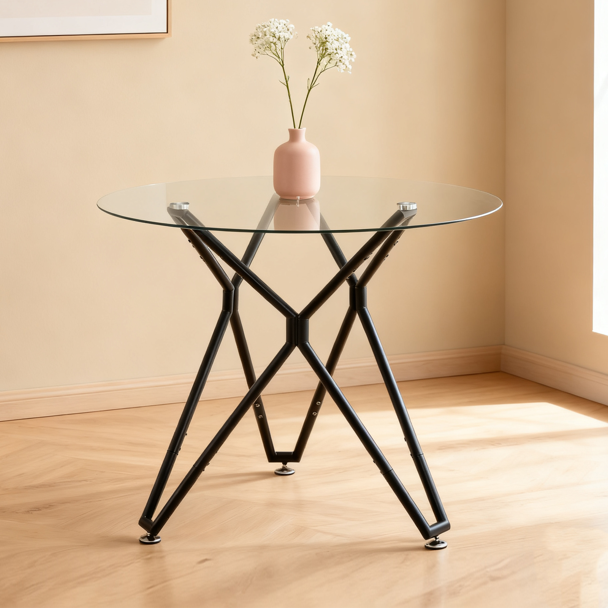 Round glass dining table with black metal base and a pink vase in a sunlit corner